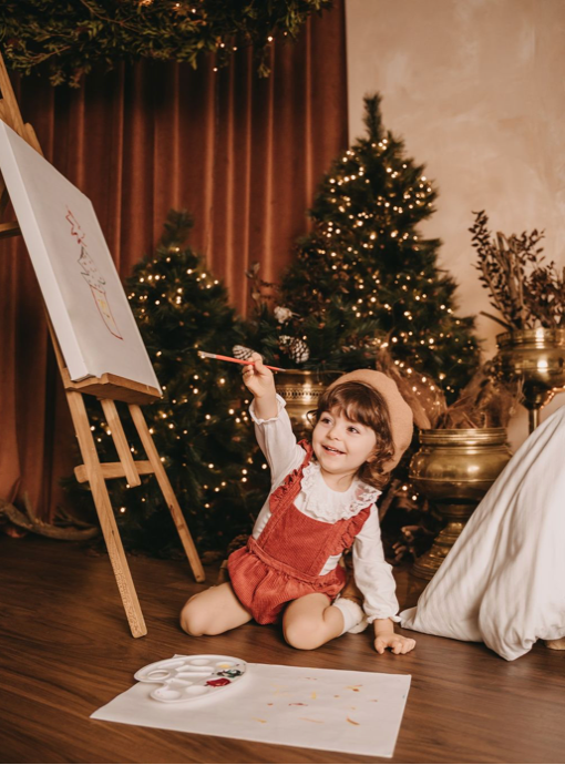 Christmas scene with decorated tree, easel, and art supplies in warm lighting.