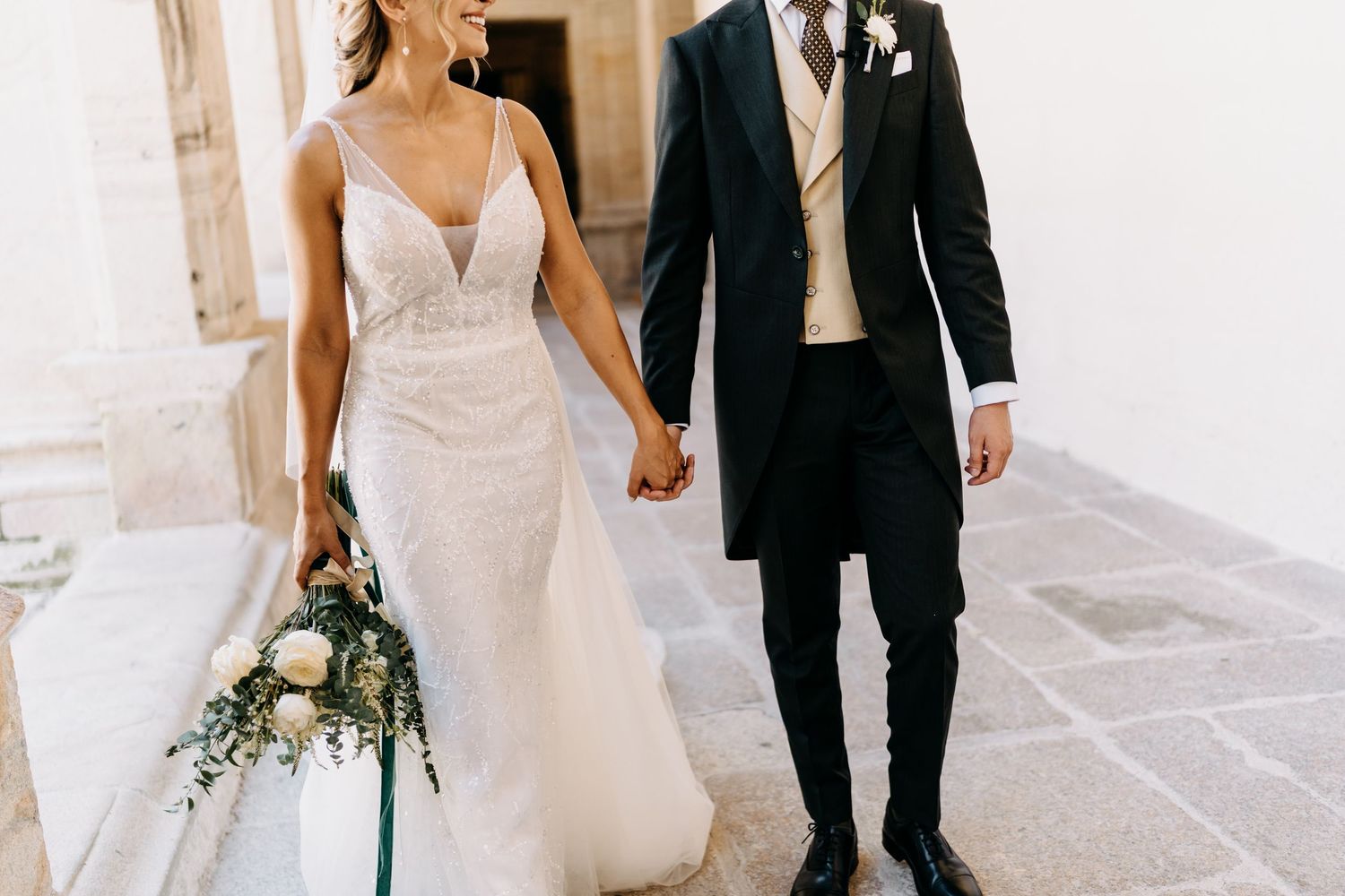 Black and white formal attire wedding couple walk down open air hallway at sunset ceremony.