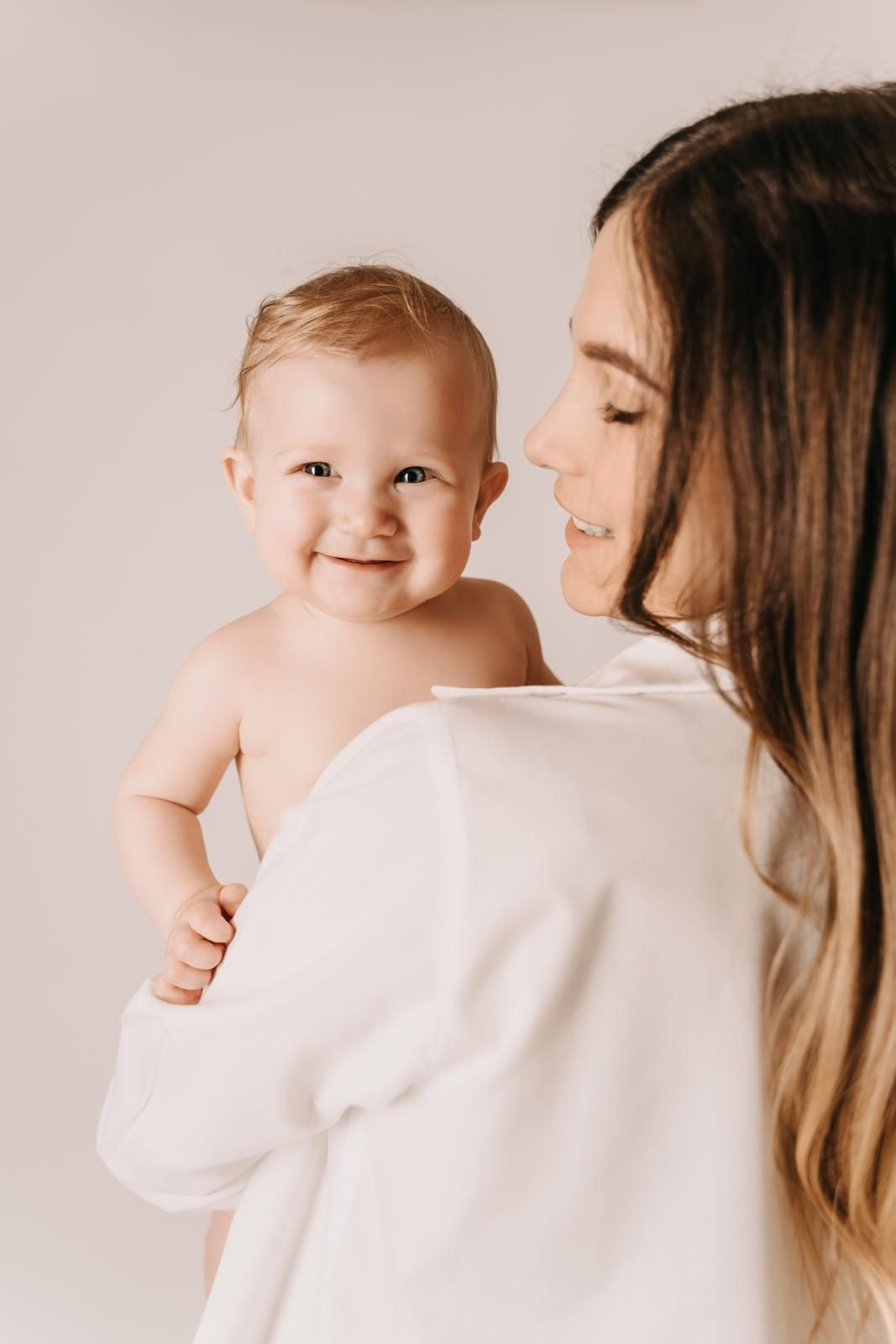 Tender maternal moment captured against light background in minimalist style.