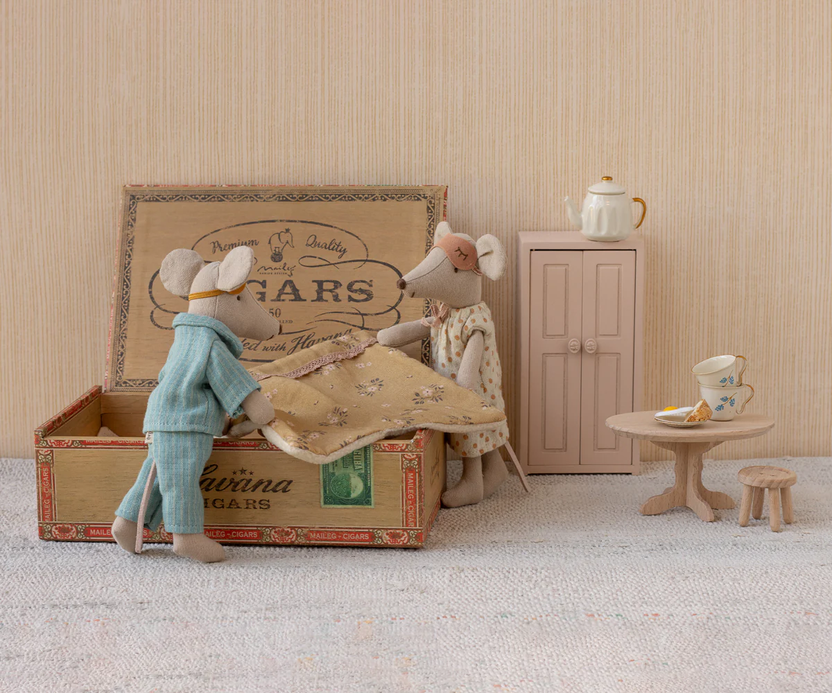 A miniature diorama shows a figure in blue examining a patient on a bed made from a vintage cigar box.