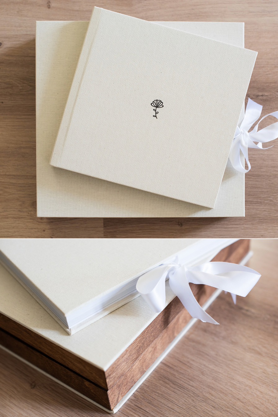 Elegant white wedding album book with small black rose icon and white ribbon binding on wooden surface.