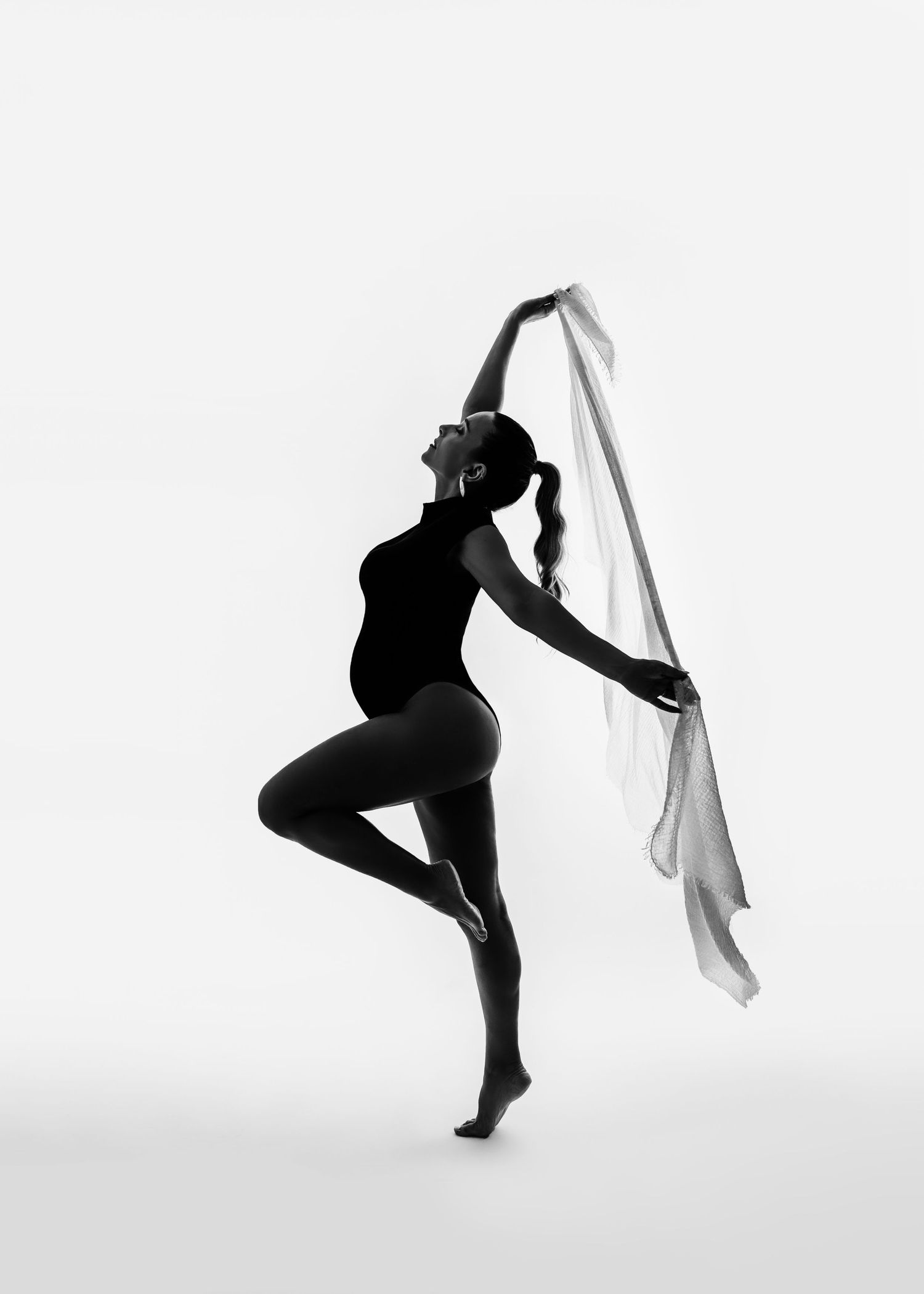 Black and white silhouette of a dancer posing gracefully with flowing fabric against a plain background.