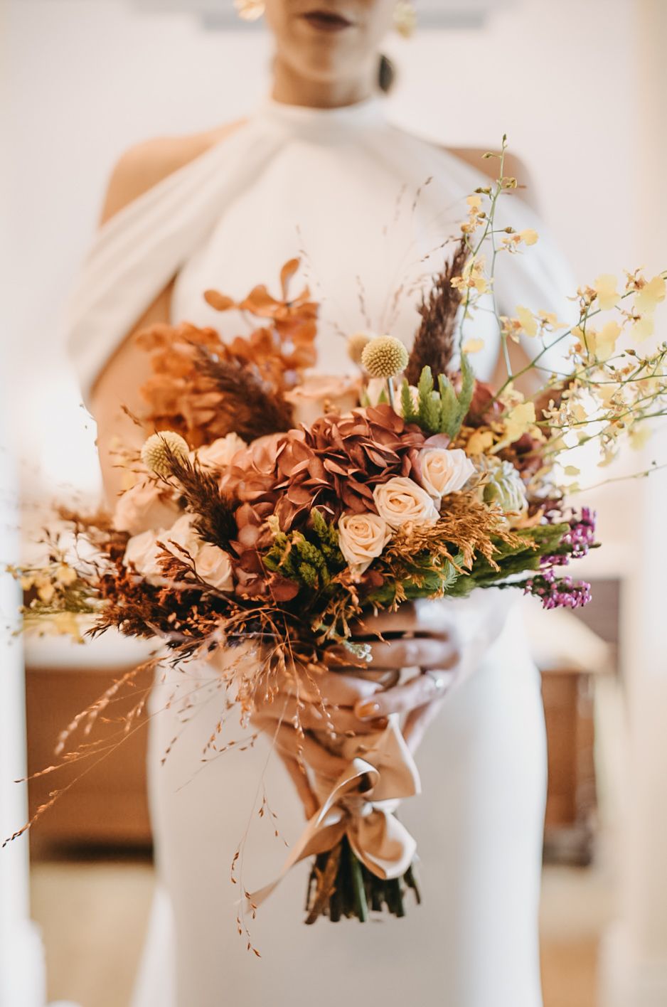 A soft, romantic floral arrangement with dried hydrangeas and roses in muted peach tones sits in a white vase.