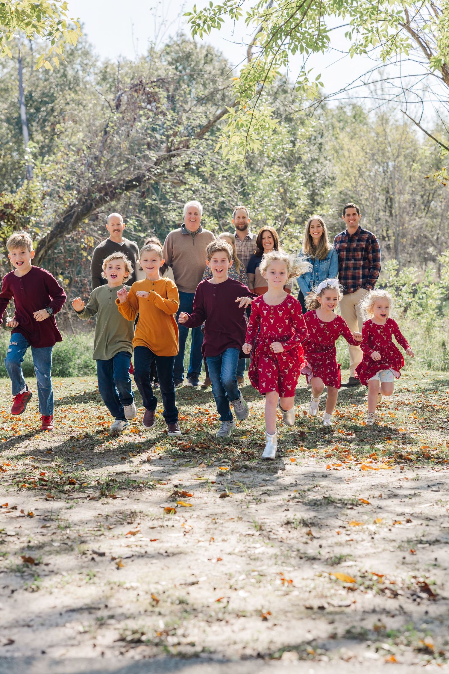 Large multigenerational family with children running toward camera in autumn park with colorful fall foliage during Houston family photos.