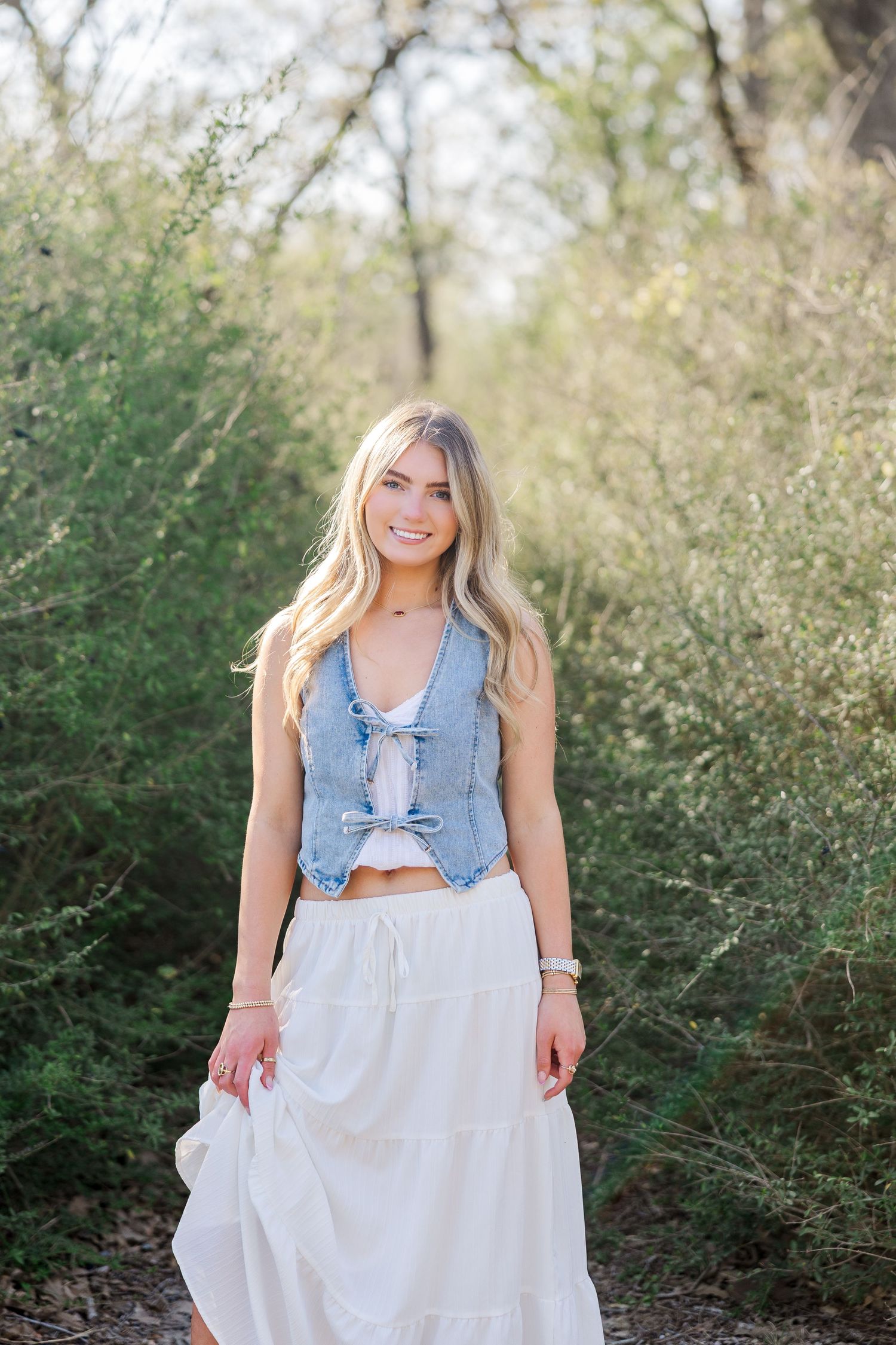 A young woman wears a denim top & white skirt outdoors during a Houston senior photography session.