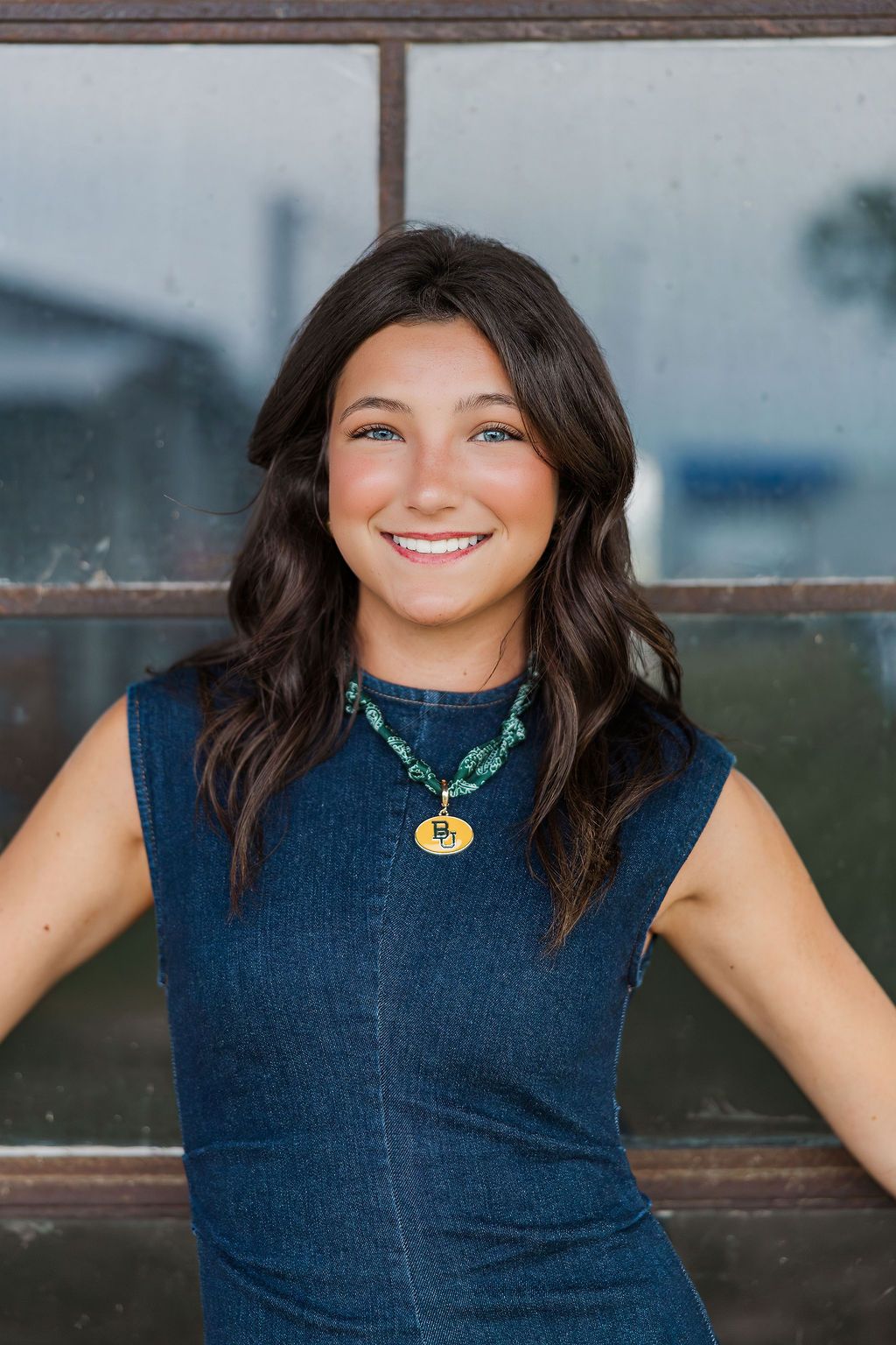 Smiling young woman with dark hair wearing a denim dress and turquoise necklace, posing outdoors for senior photos in Houston.
