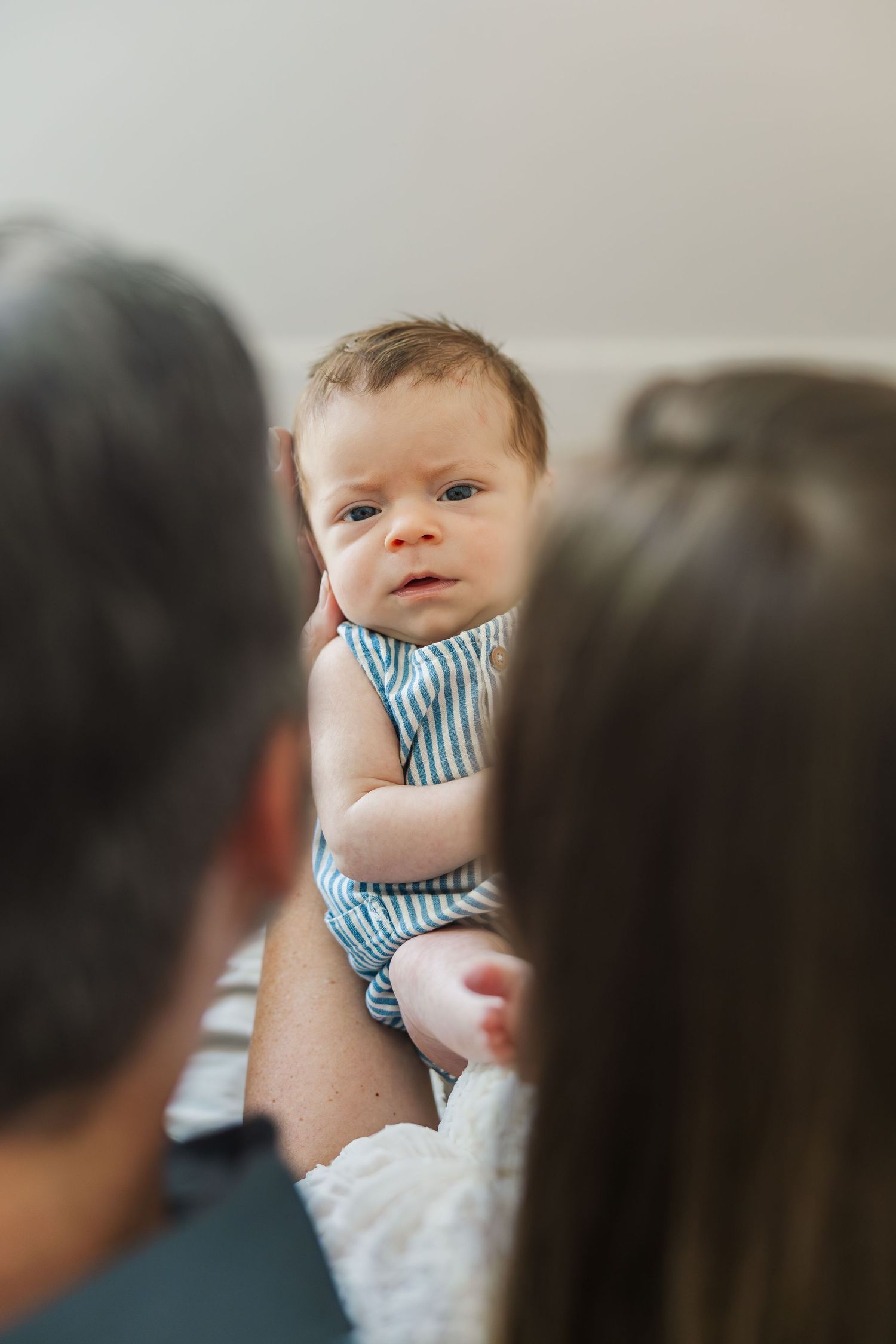 Newborn baby in striped onesie being held by parents, looking curiously at the camera during a Houston newborn photography session.