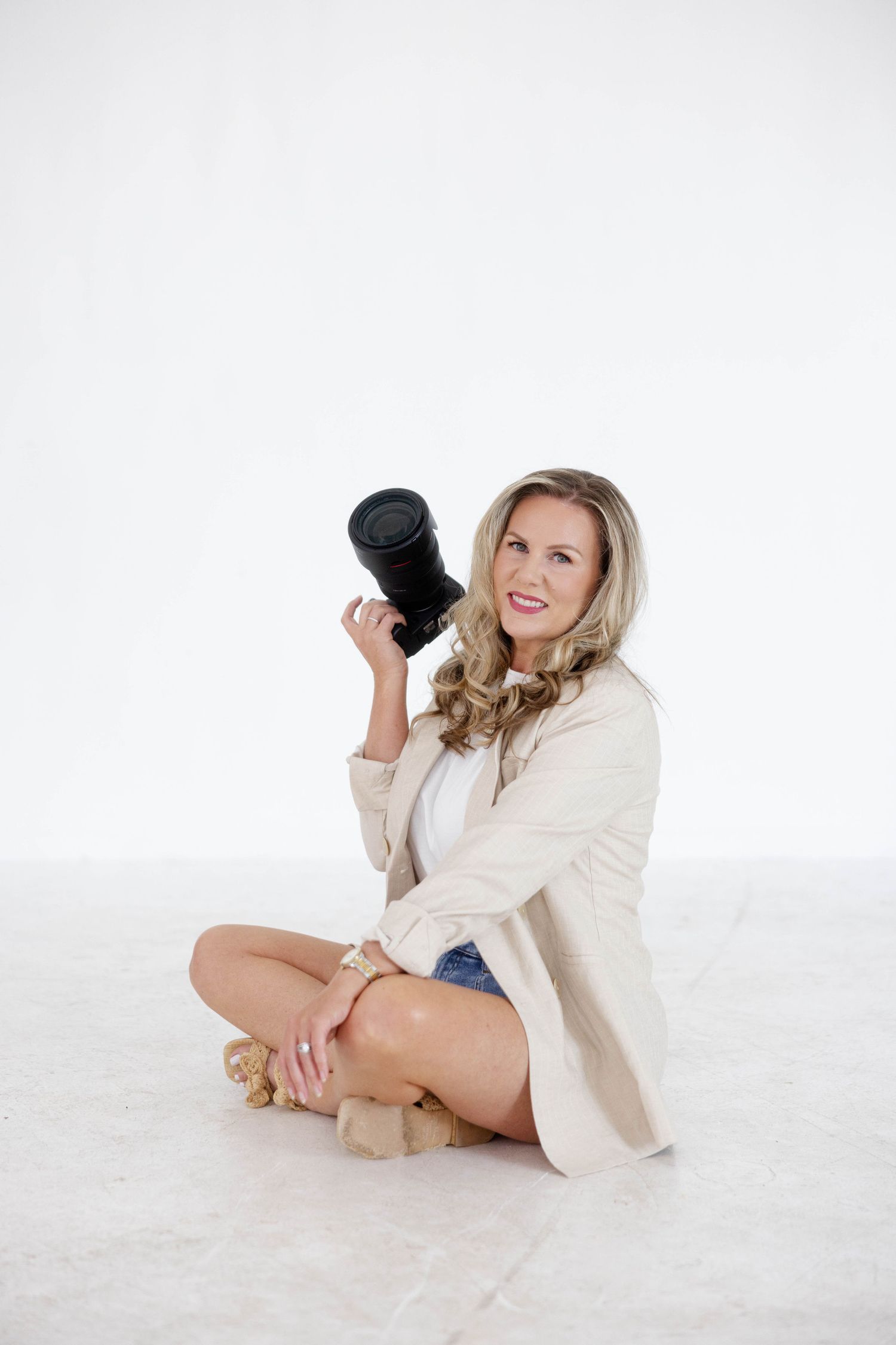 The Houston senior photographer behind Carla Collins photography is seated before a white background, wearing a beige blazer.