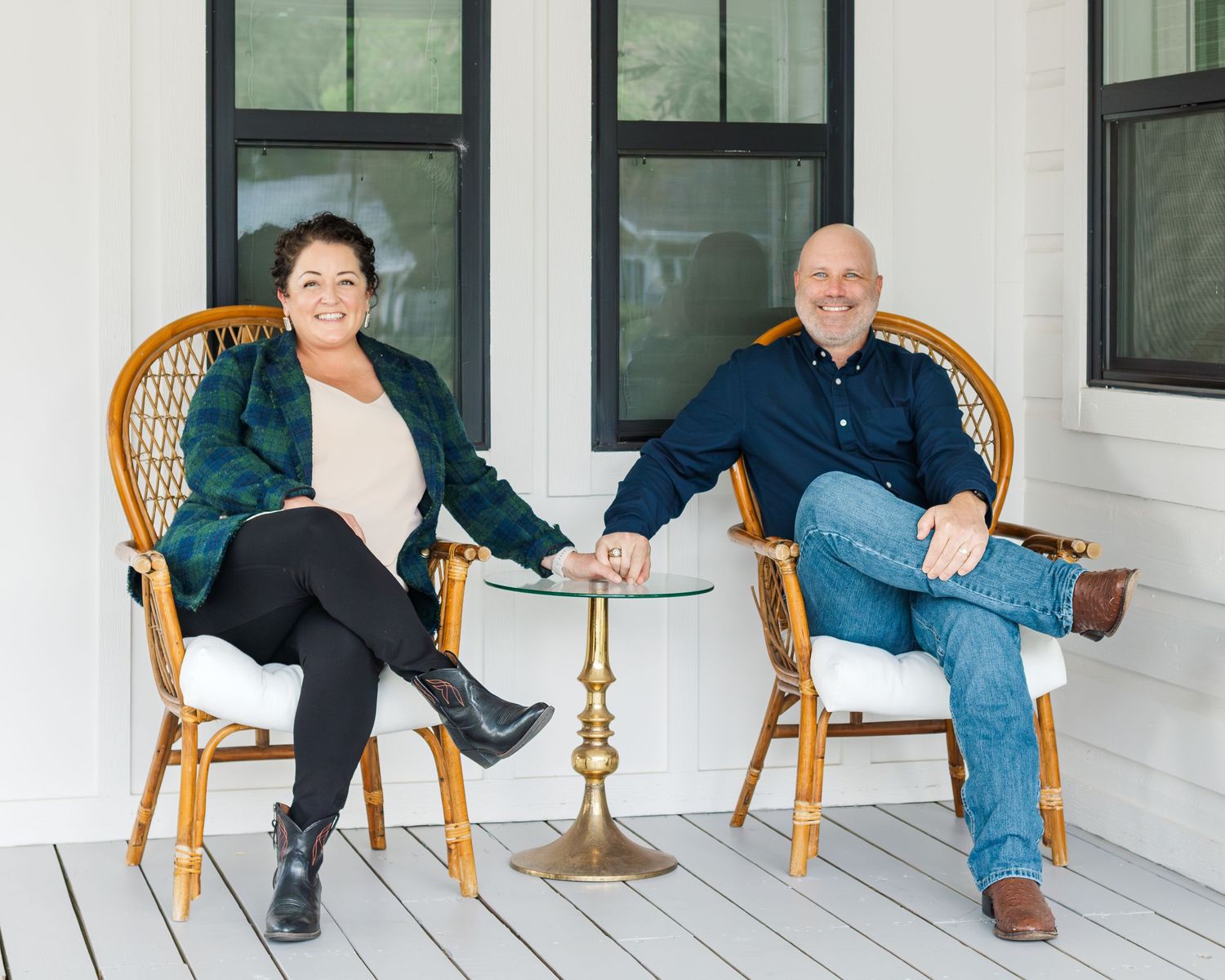 Two people sitting in wicker chairs on a white porch having a conversation.