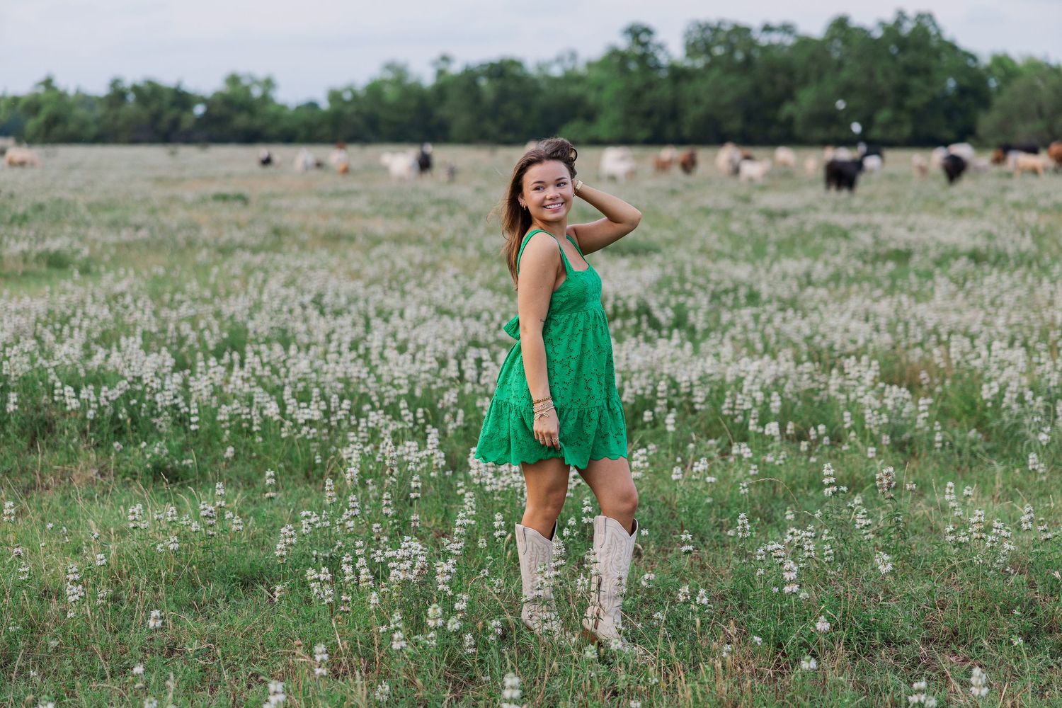 A smiling young woman in a green dress and cowboy boots poses during a session with a Houston senior photographer.