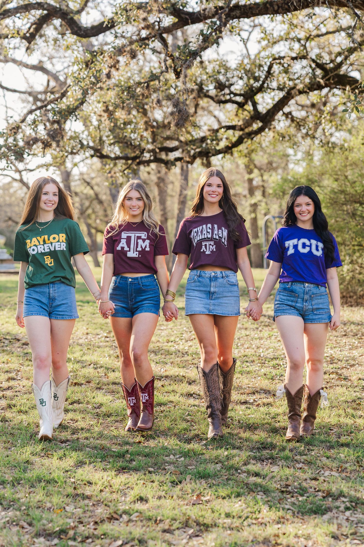 Four girls in Texas university shirts and cowboy boots hold hands walking outdoors during senior pictures in Houston.