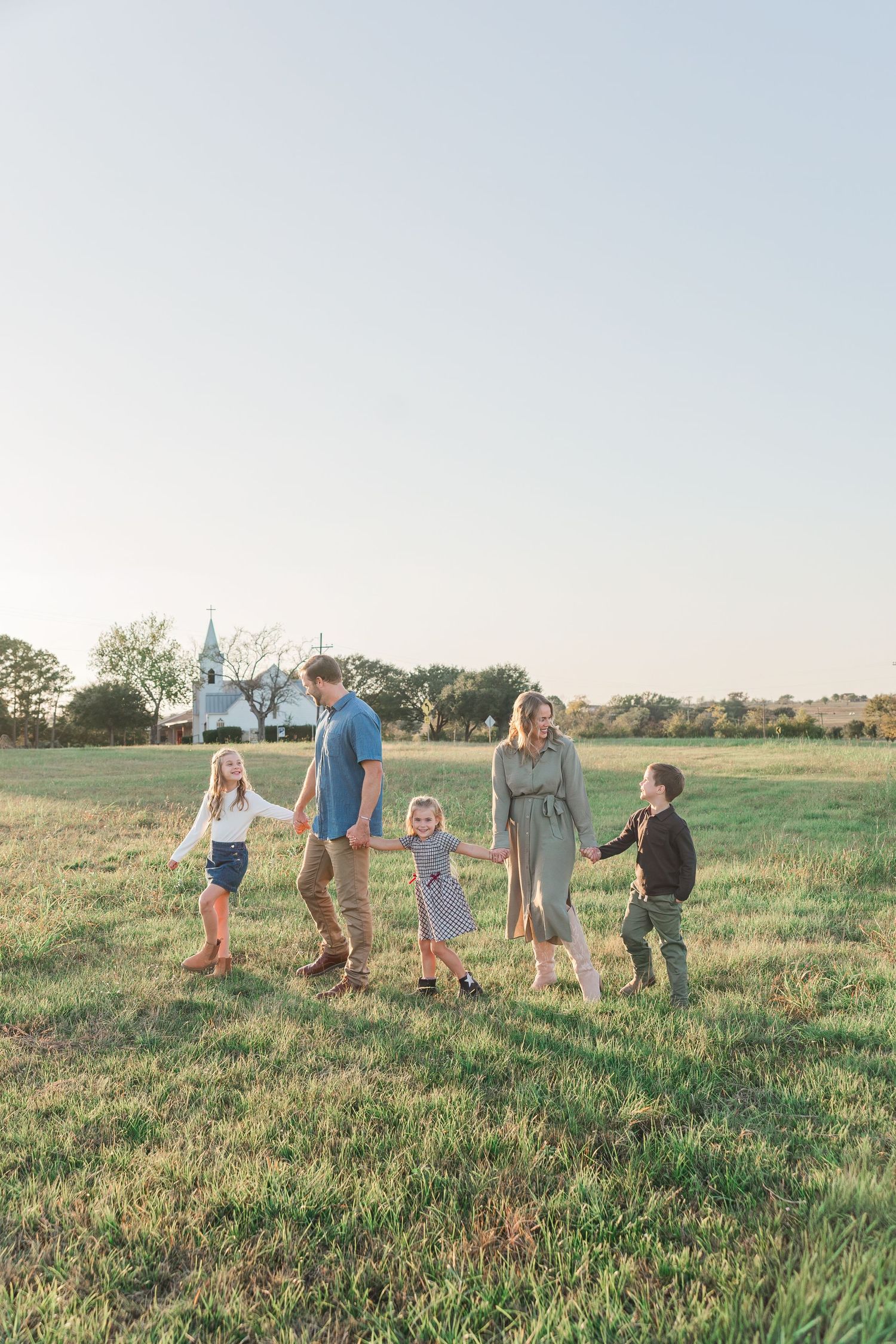 Family of five holding hands walking through a green field at golden hour in a photo taken by a Houston family photographer.