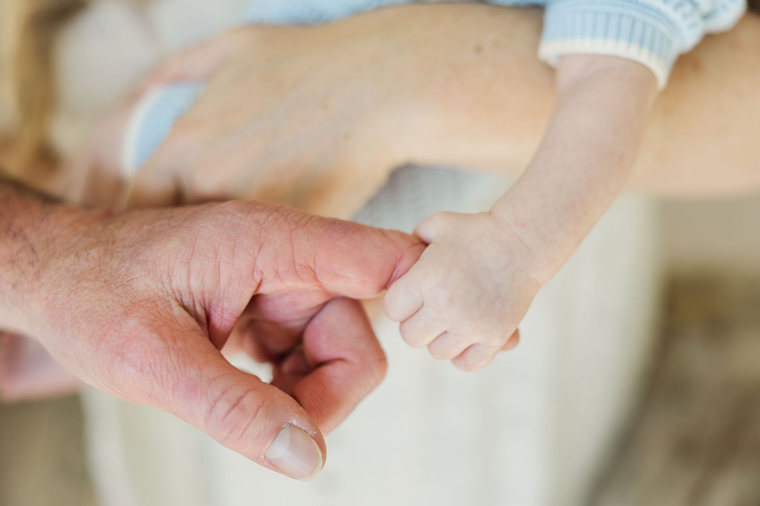 A baby's tiny hand gently gripping an adult's finger during a Houston newborn photography session.