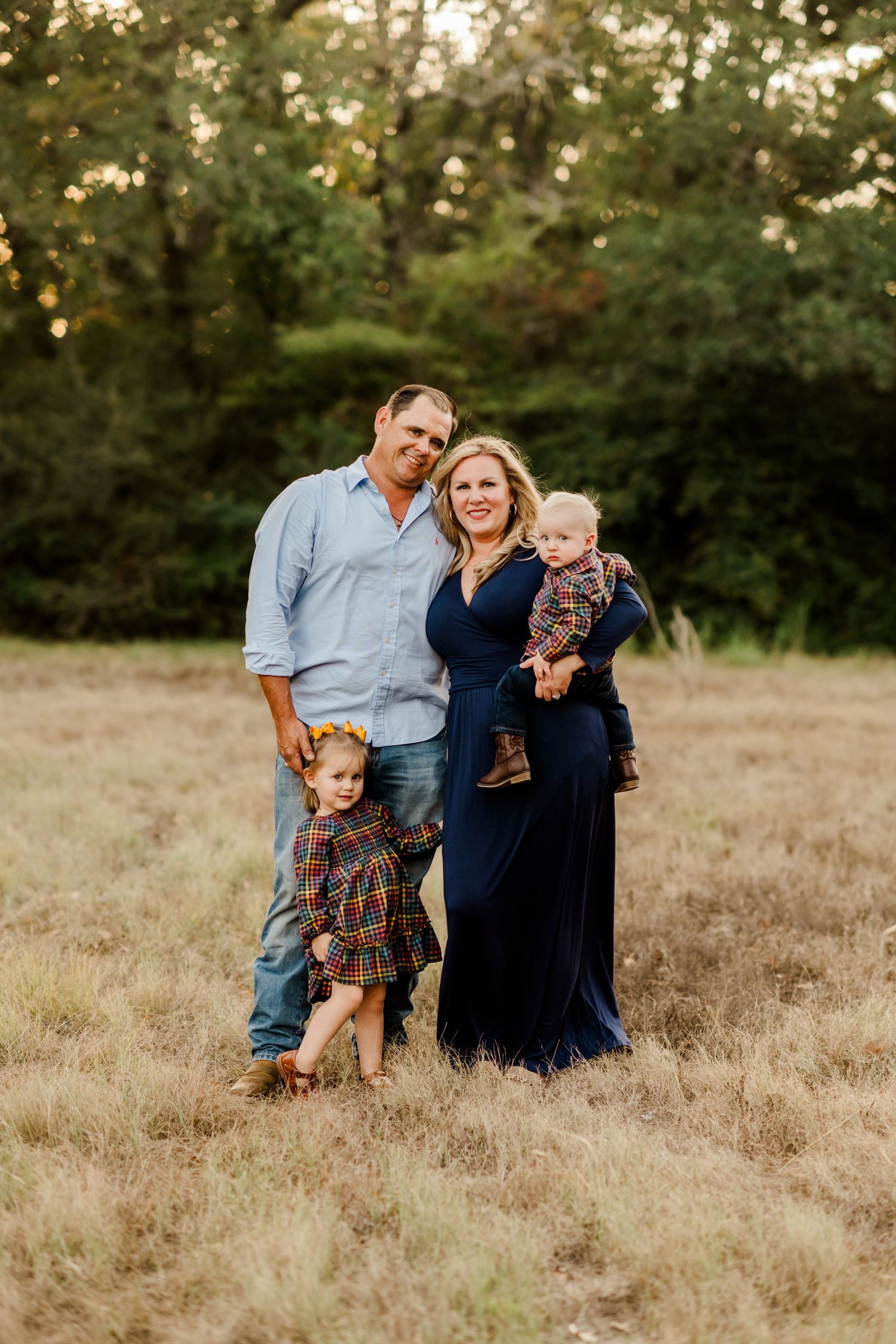 A family poses together in a field during golden hour wearing coordinated navy and plaid outfits.