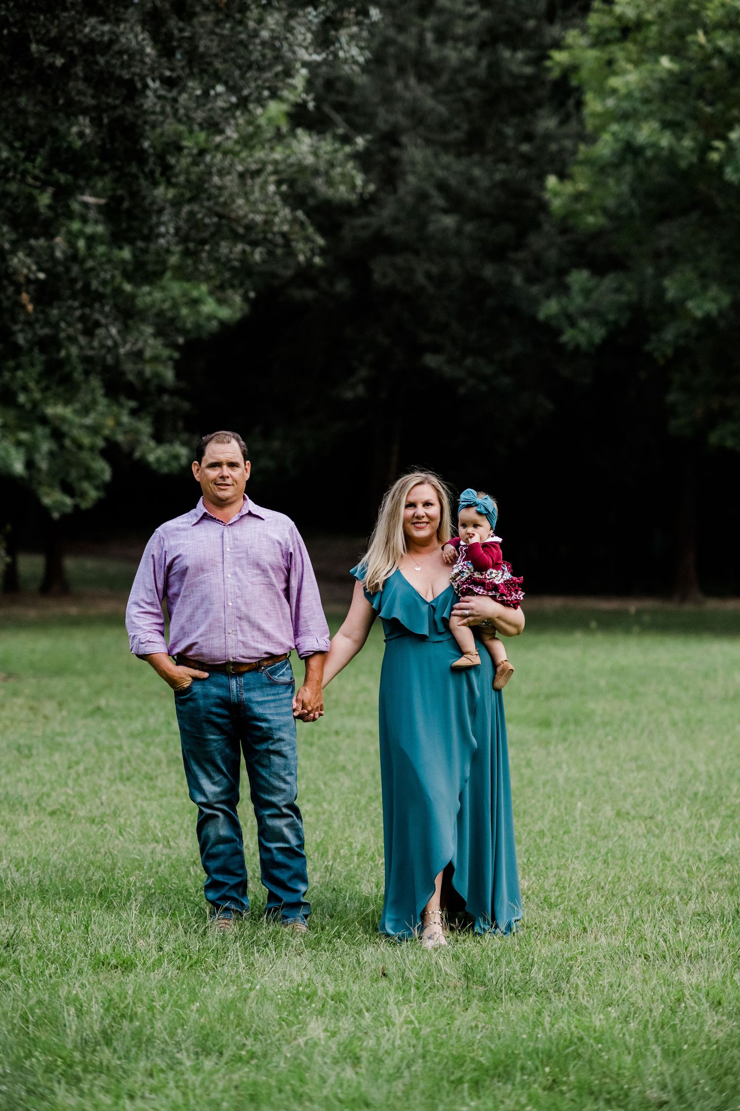 A family stands together in a grassy field, with the woman wearing a teal maxi dress.