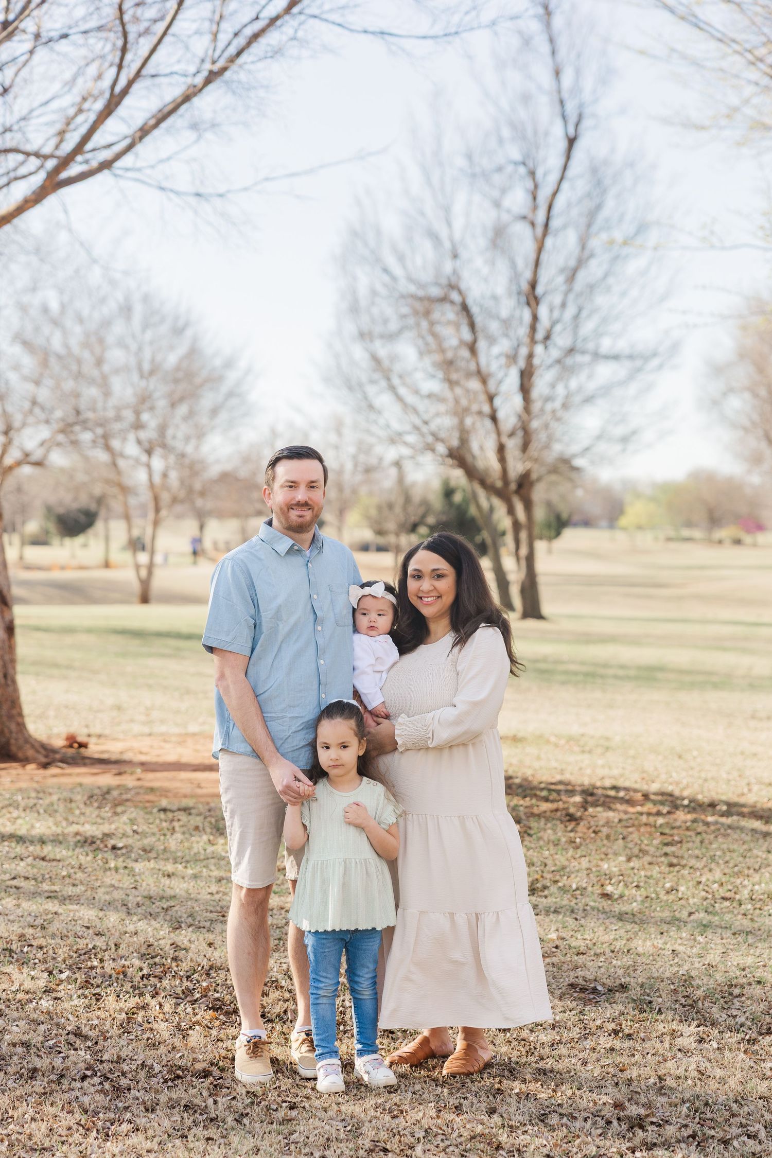 A Texas family of four smile in a field in early fall during Houston family photos.