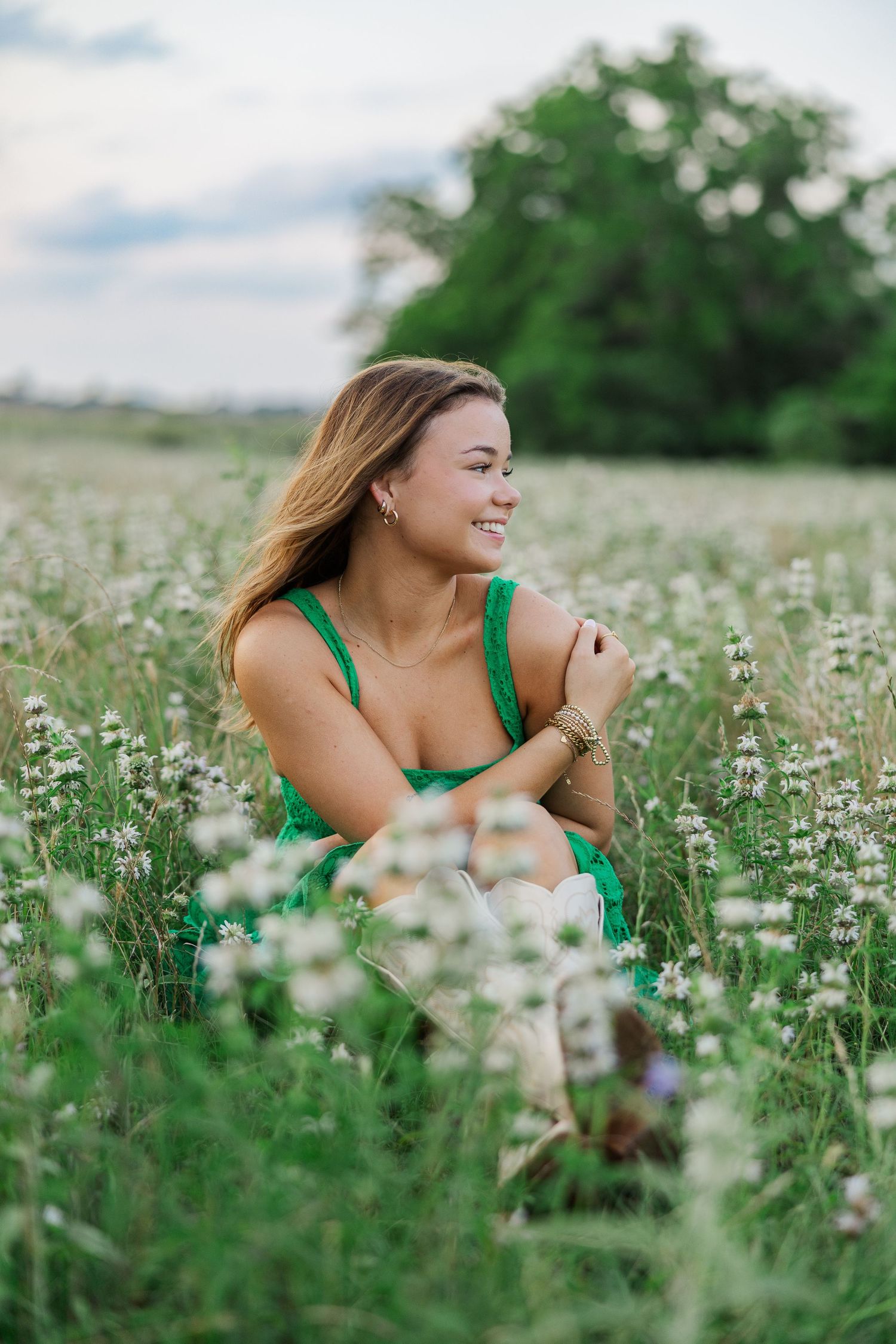 Smiling young woman in green dress sitting among wildflowers during a photoshoot with a Houston senior photographer.