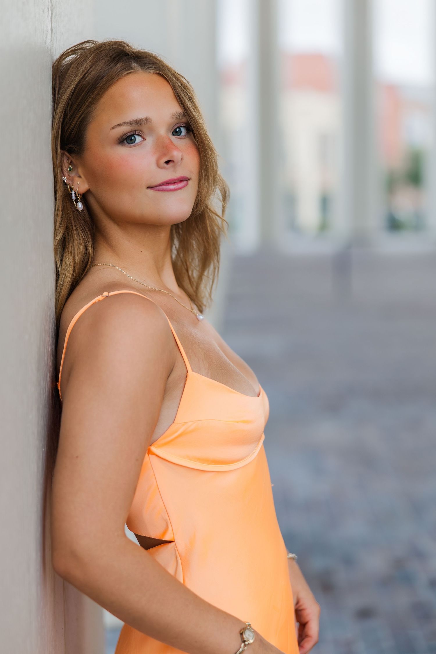 Young woman in peach satin slip dress leaning against a column during a Houston senior photography session.