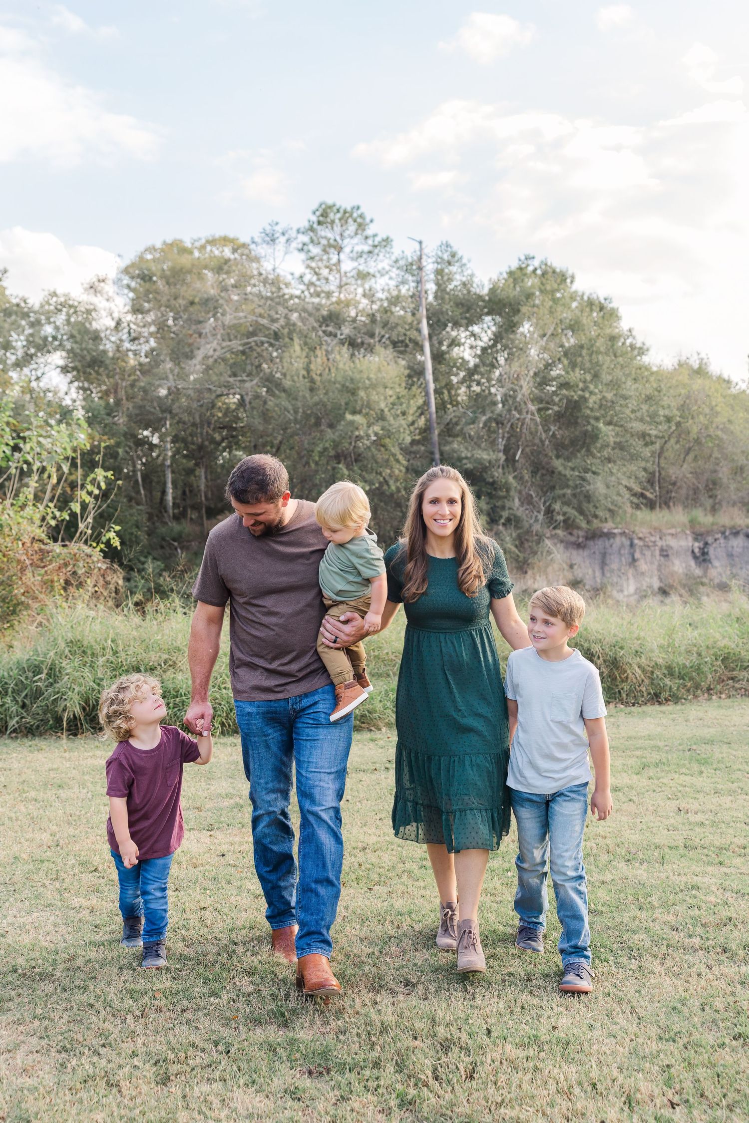 Family of five walking outdoors on green grass, parents with three young boys in casual Houston TX fall family portrait.