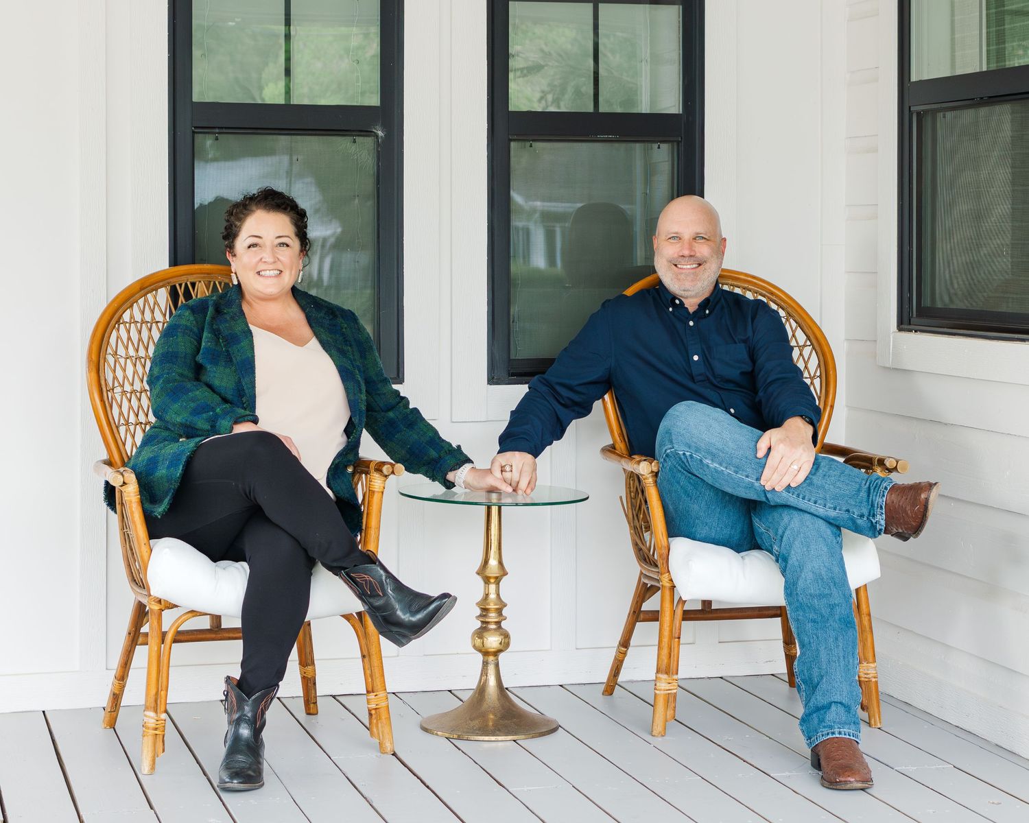Two smiling adults sit in wicker chairs on a white porch, posing together beside a small gold accent table during Houston family photos.