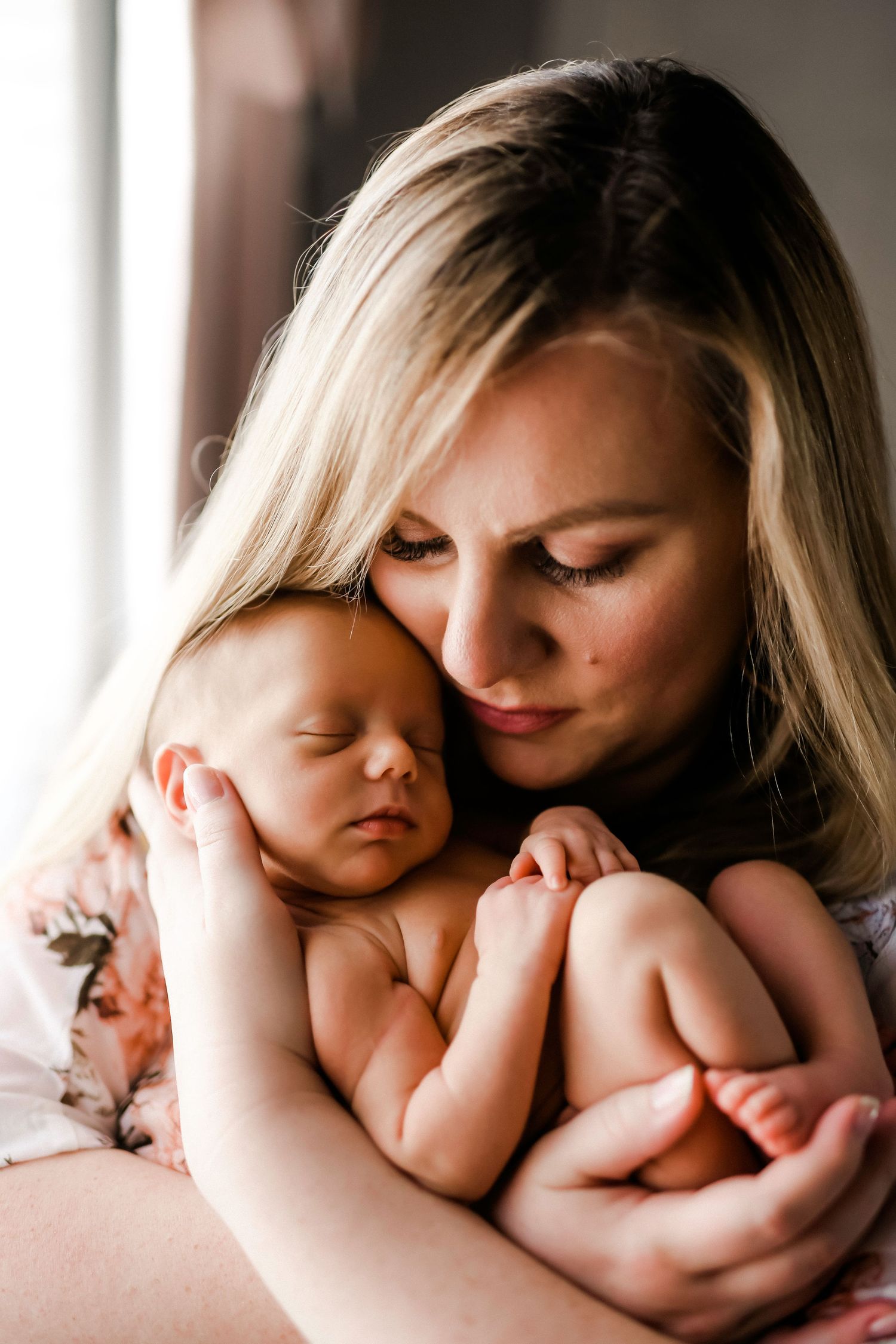 An intimate portrait of a parent holding a sleeping newborn baby in natural window light.
