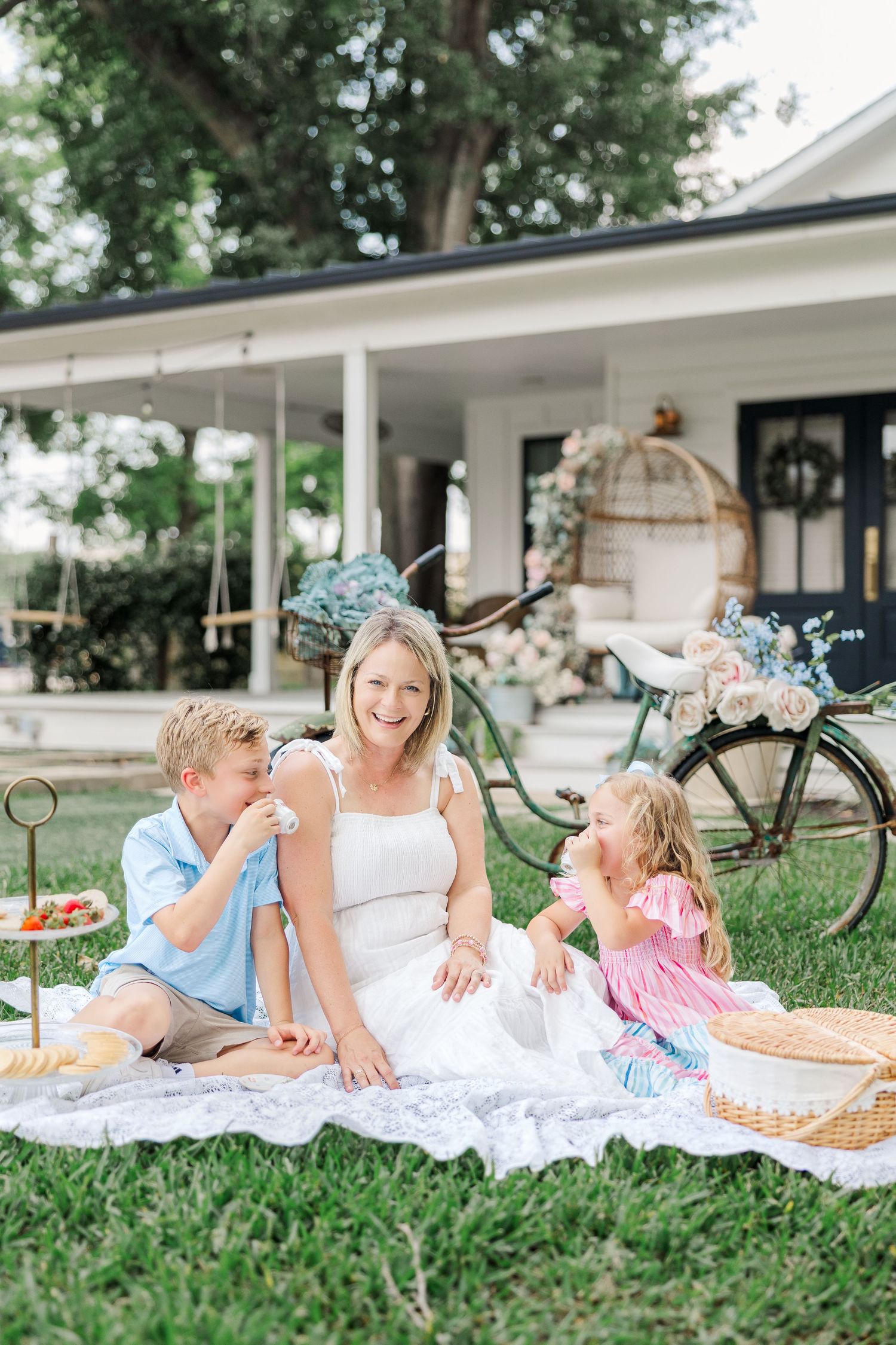 A woman smiles with two young children on a white blanket during a photoshoot with a Houston newborn & family photographer.