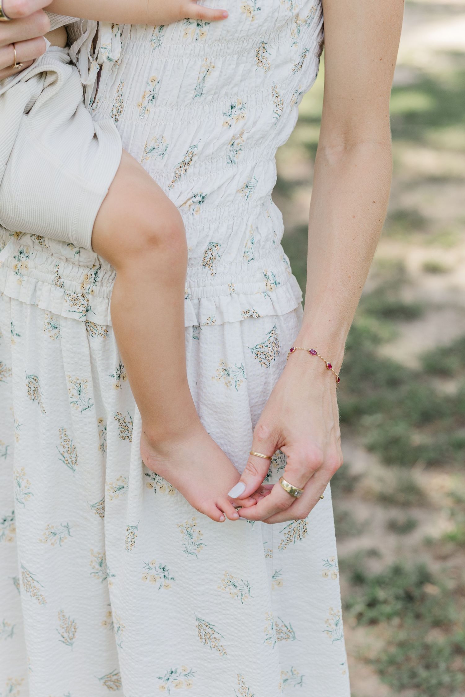 Woman in floral white midi dress touches her baby's foot during a milestone session with a Houston newborn photographer.