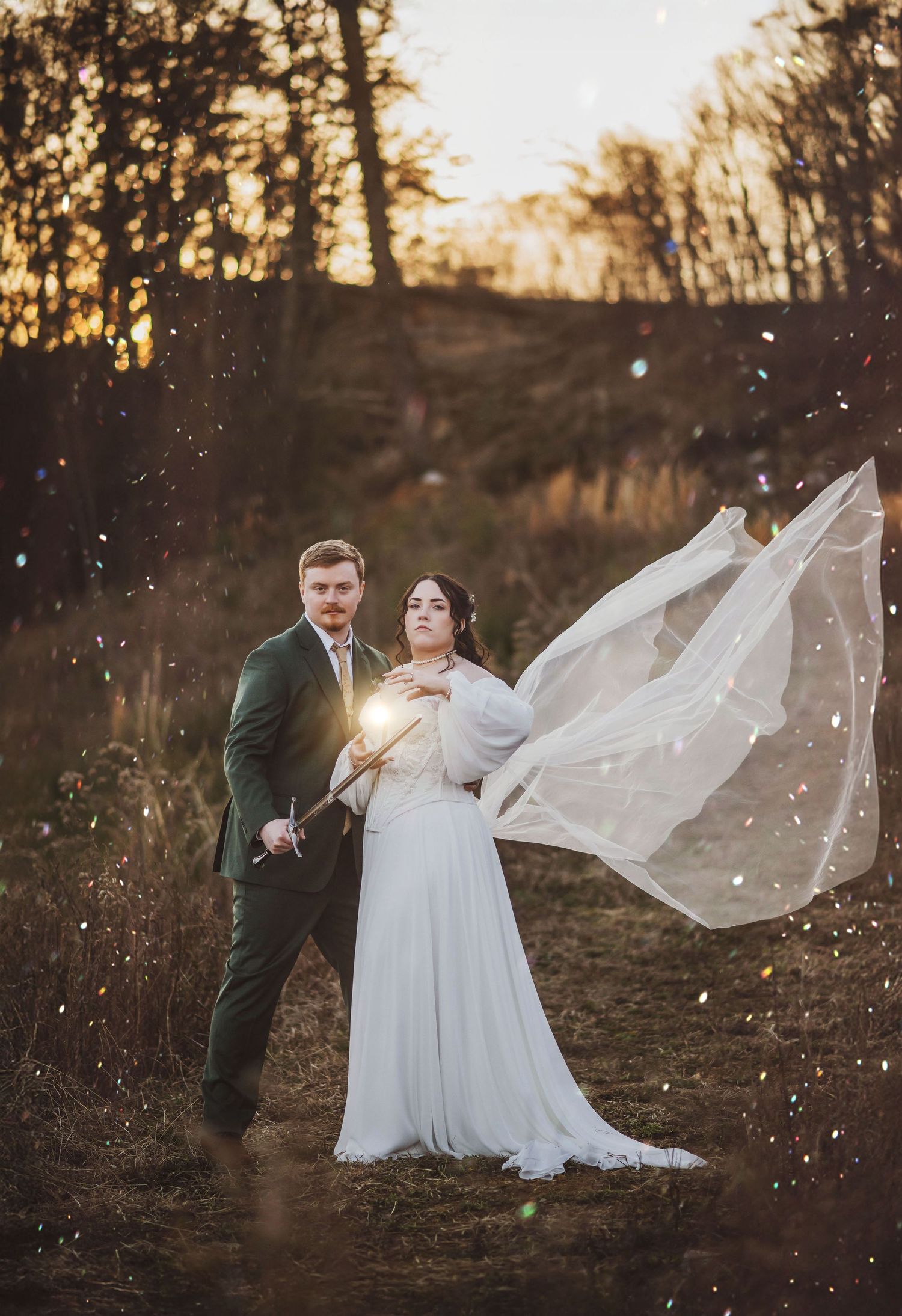 A winter wedding couple stands on a forest path at sunset as a flowing veil catches the golden light and falling snow.