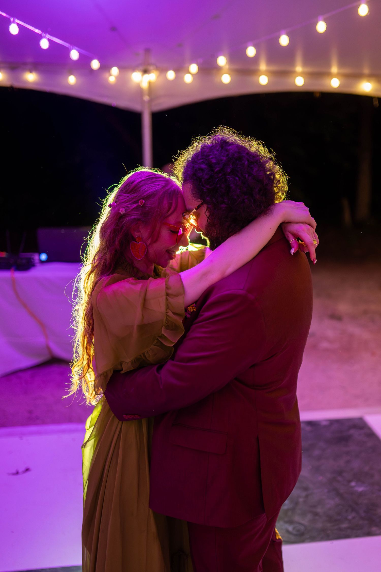 Couple sharing an intimate first dance under string lights at an outdoor evening wedding reception.