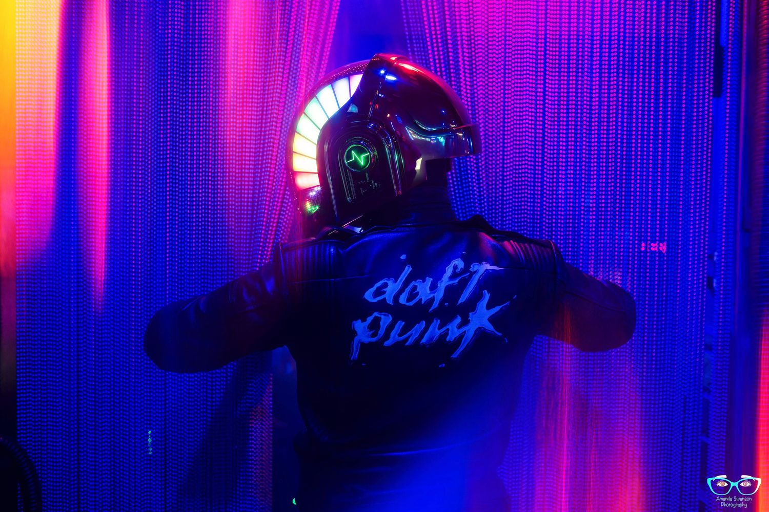 A figure wearing a glowing LED helmet and dark jacket stands against vibrant purple and pink lighting streaks.