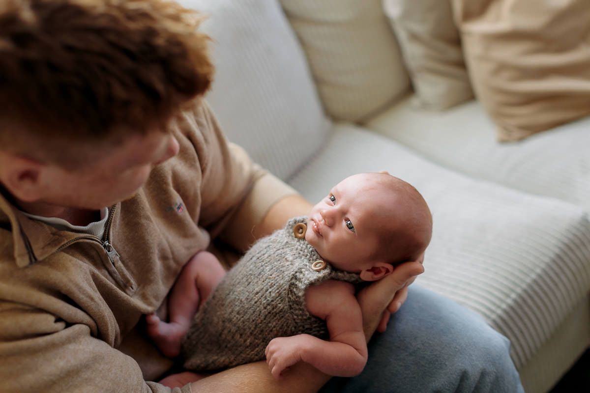 Nyfødt gutt ligger i armene til pappa og ser opp på han.