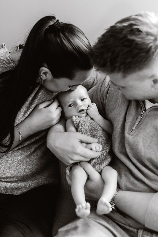 Svart-hvitt bilde av mamma og pappa som holder sin nyfødte sønn. Mamma kysser ham på hodet og pappa ser på ham.