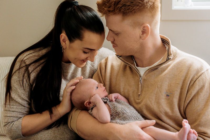 Mamma ser på gutten sin som ligger i armene til pappa. Pappa ser på mamma med kjærlighet i blikket.