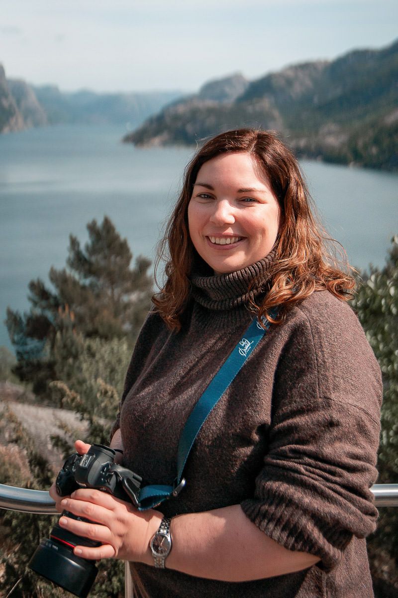 Portrett av fotograf Tone Ørstavik fra Ørstavik Foto. Hun står med utsikt til Lysefjorden bak seg og smiler til kamera.