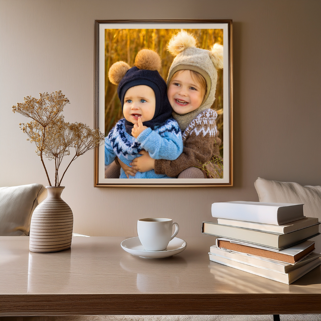 Mockup bilde av et veggbilde av søster og bror i solnedgang, over et bord med kaffe og bøker. Reklame for Ørstavik Foto sine produkter.