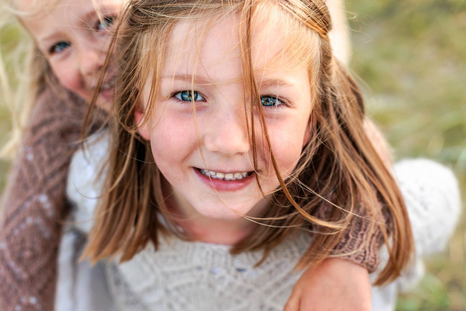 Nærbilde av storesøster med lillesøster på ryggen på Solastranda. Tatt av Ørstavik Foto, familiefotograf i Rogaland.