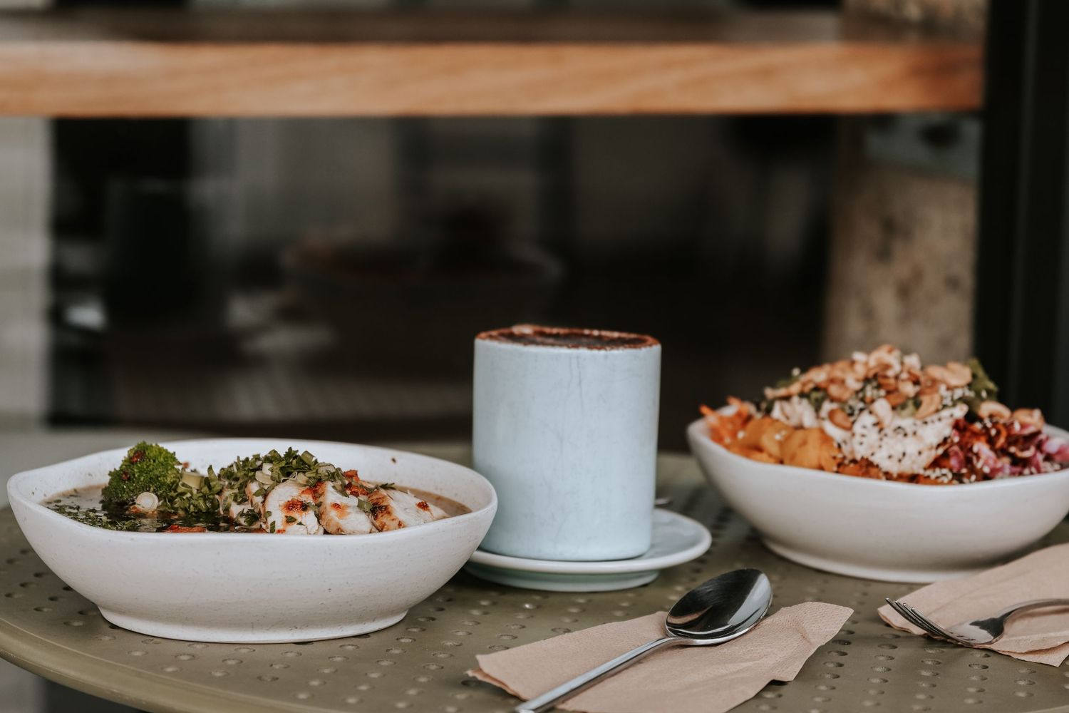 Two grain bowls and a latte on a cafe table with napkins and spoon.