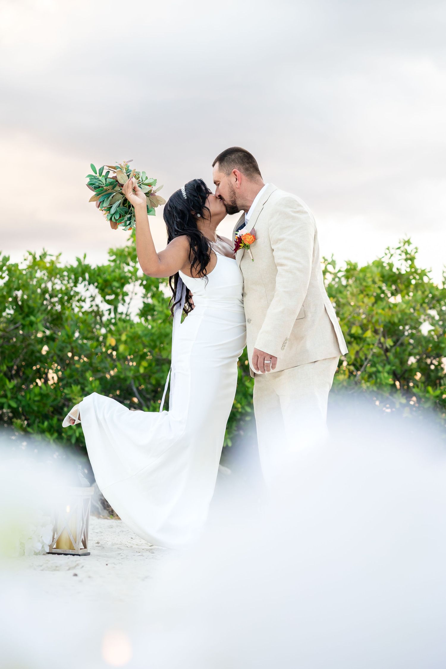 A romantic couple in wedding attire embraces in a dreamy outdoor setting with lush greenery and soft lighting.