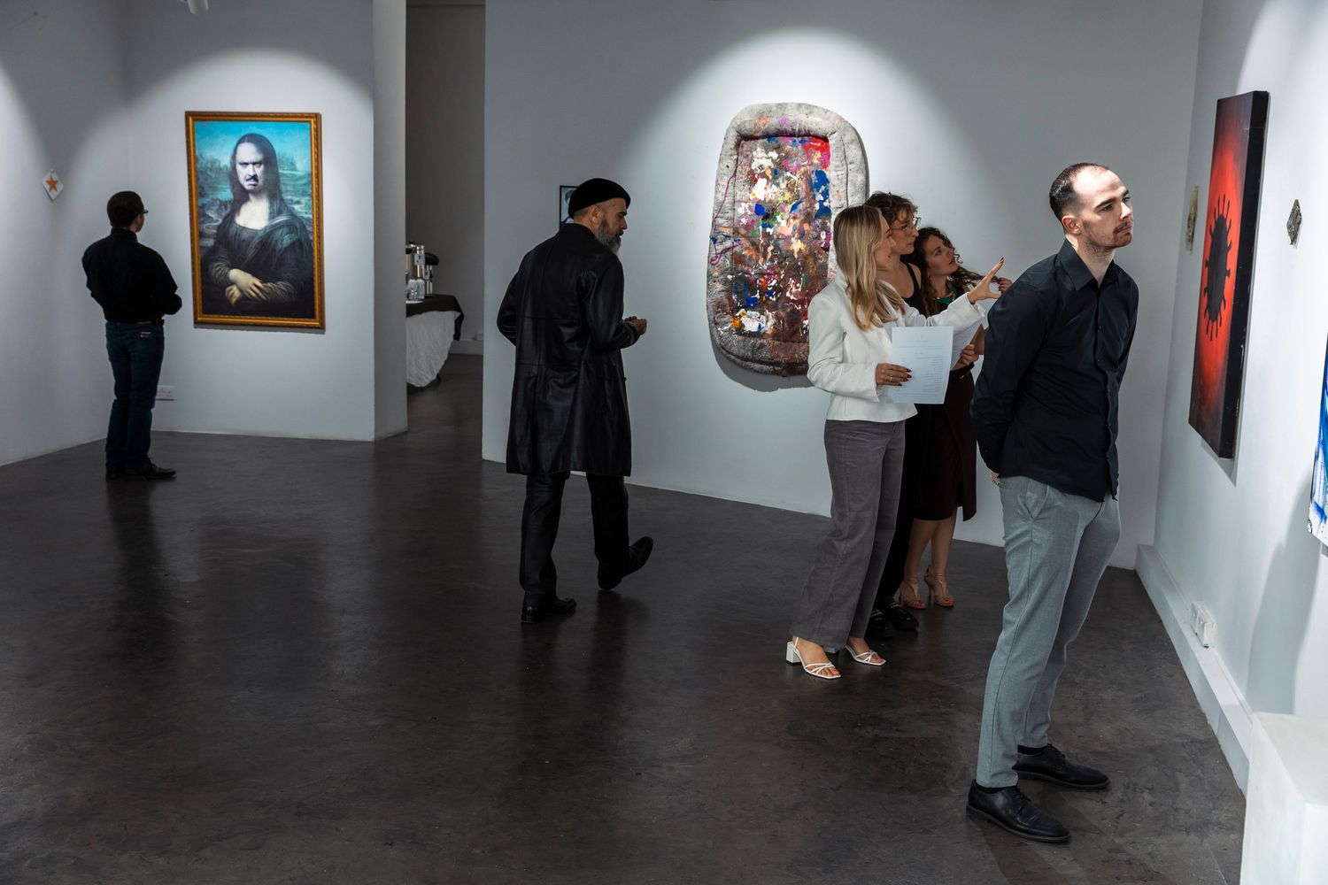 Gallery visitors view artwork displayed on white walls in a contemporary art exhibition space.
