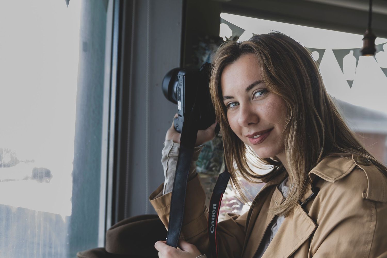 Woman in cozy sweater sits by window with coffee cup and laptop, looking thoughtfully outside.