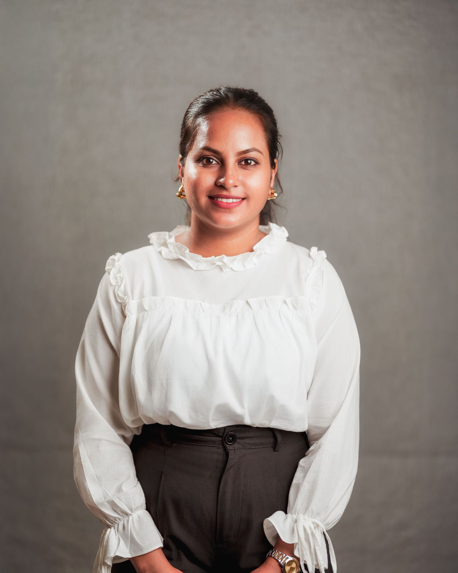 Professional portrait in white ruffled blouse and dark skirt against grey backdrop.