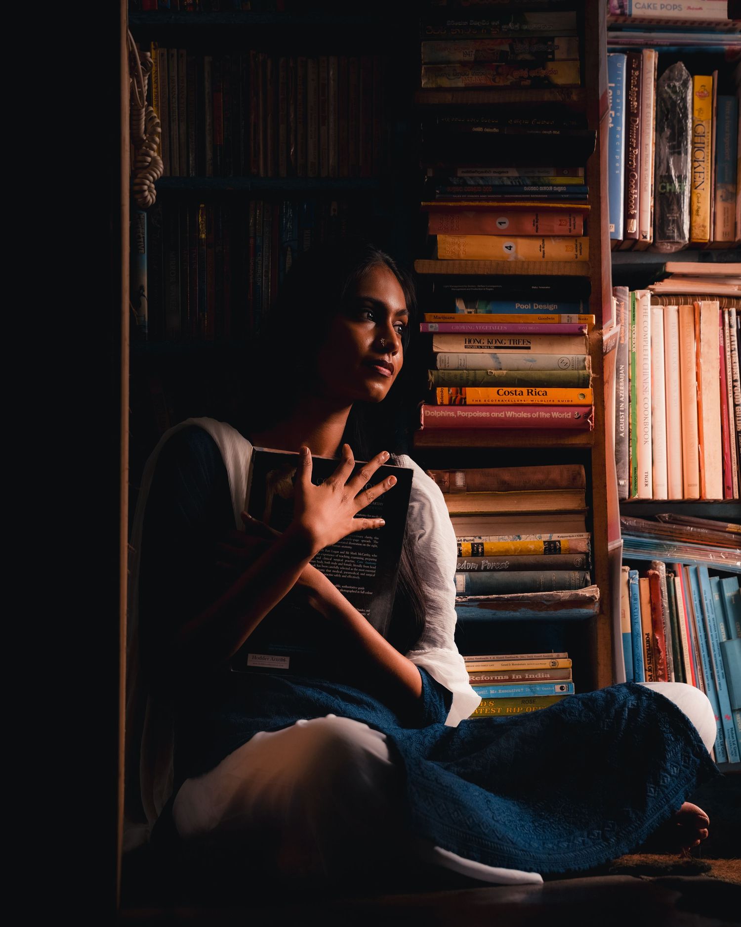 Person sitting in a dimly lit library surrounded by bookshelves.