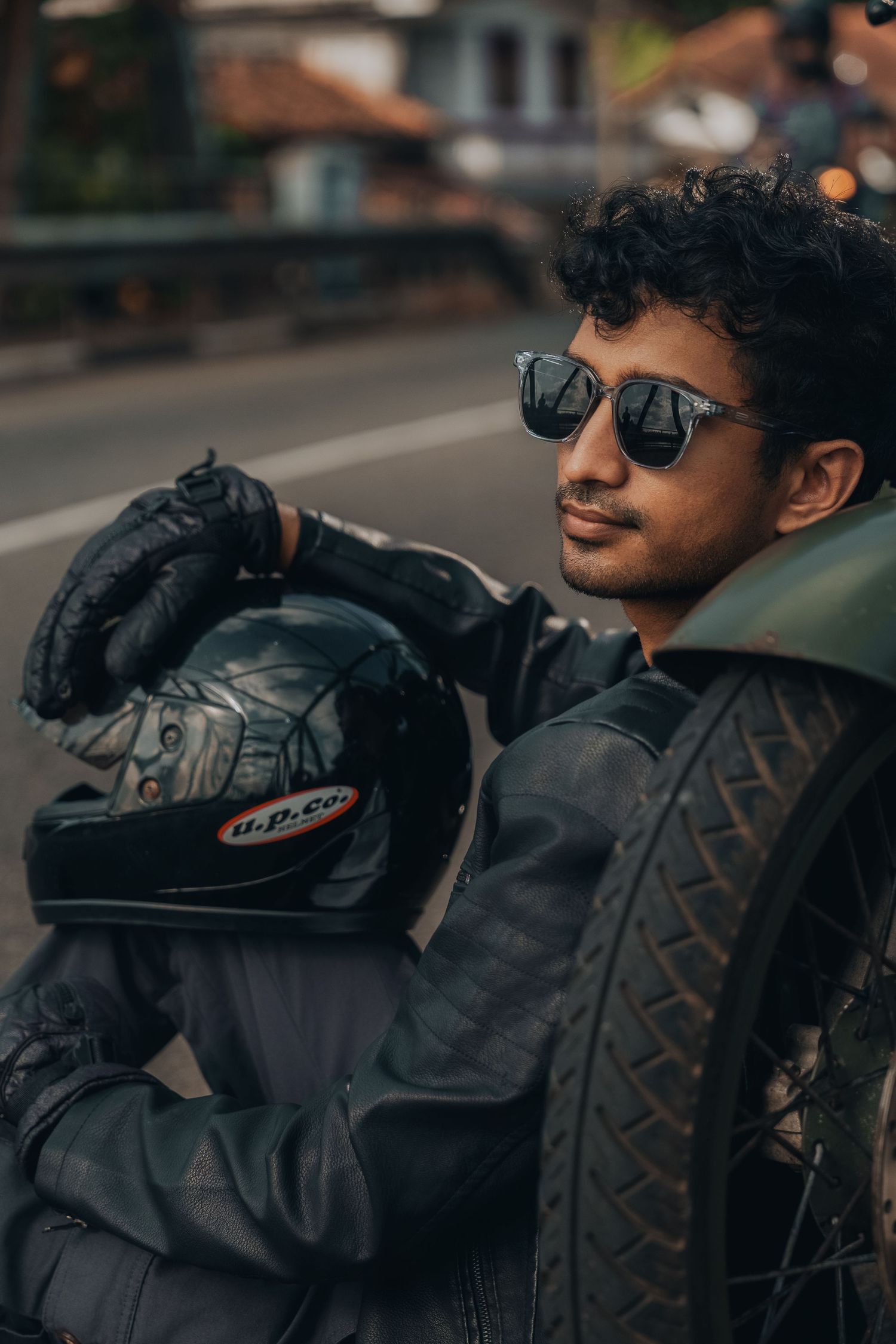Person in black leather jacket and sunglasses looking away in urban setting.
