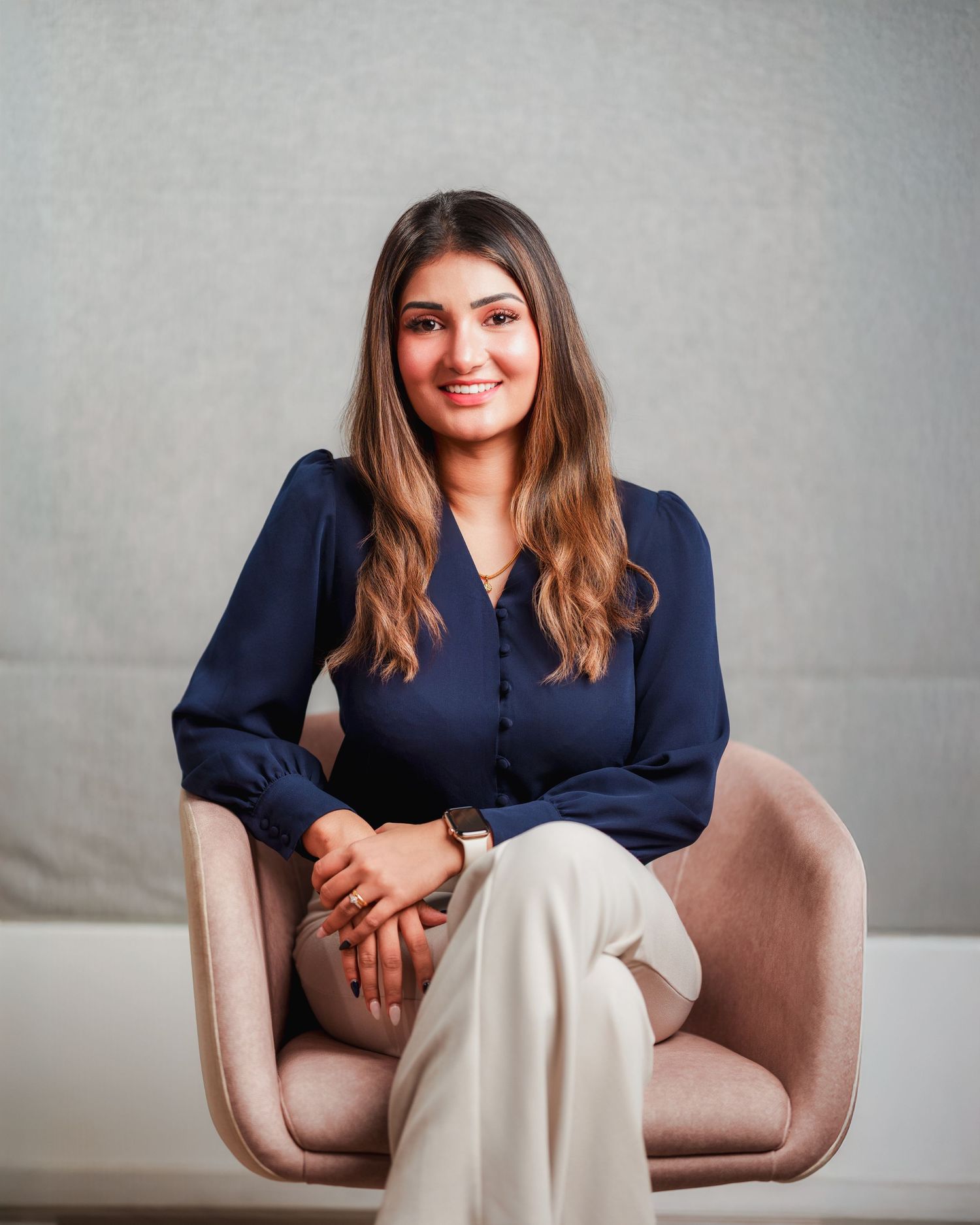 Casual business portrait seated in armchair wearing navy blouse and cream pants.