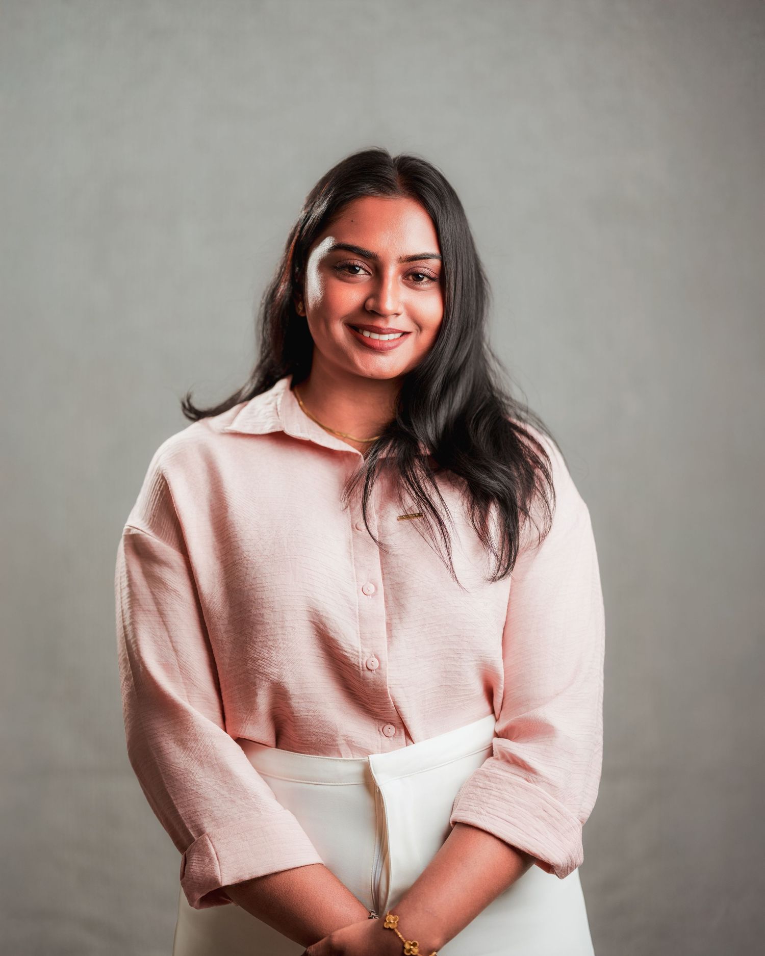 Casual business portrait in soft pink button-up top against grey studio background.