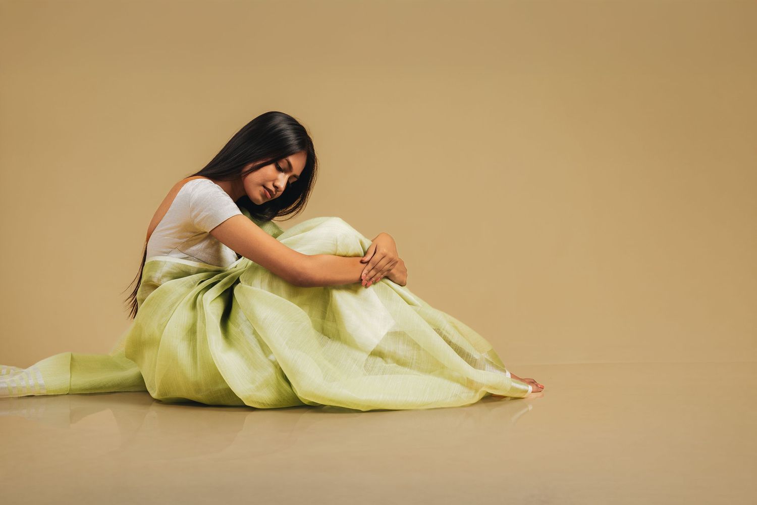 Model in flowing pale yellow dress reclines gracefully on studio floor.