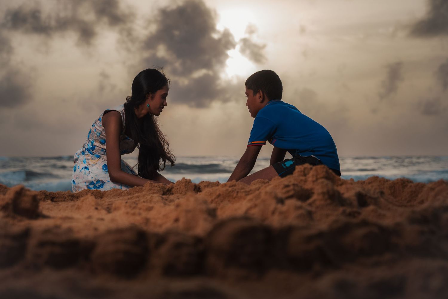 Children building sandcastles on a beach at sunset with dramatic cloudy skies.
