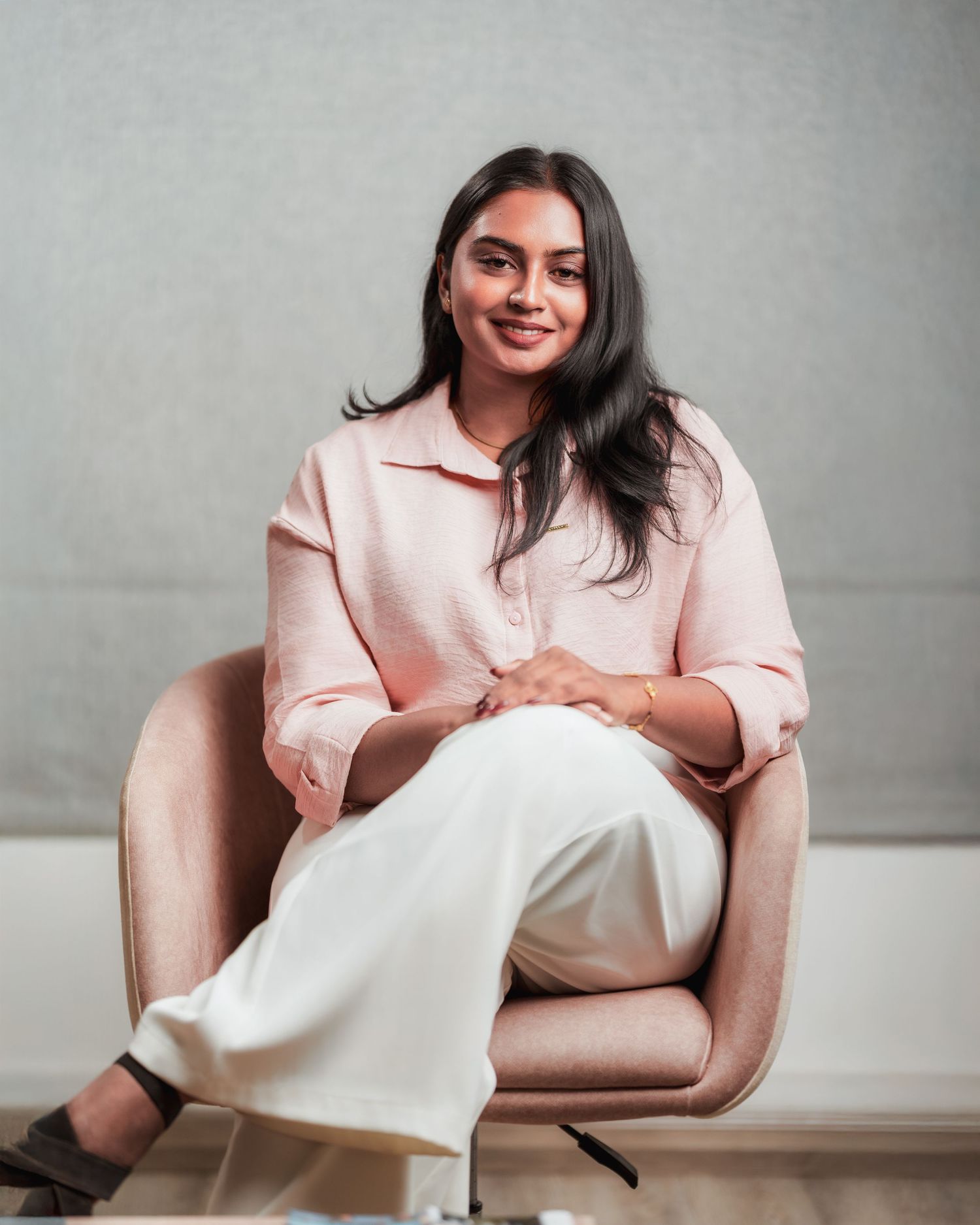Professional headshots featuring person in light pink blazer seated in modern setting.