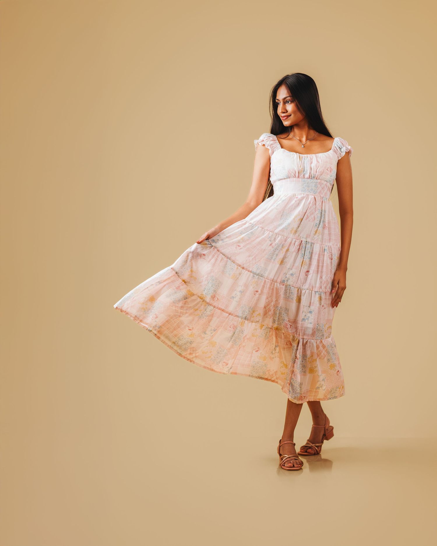 Model twirls in flowy pink floral sundress showing movement against beige background.