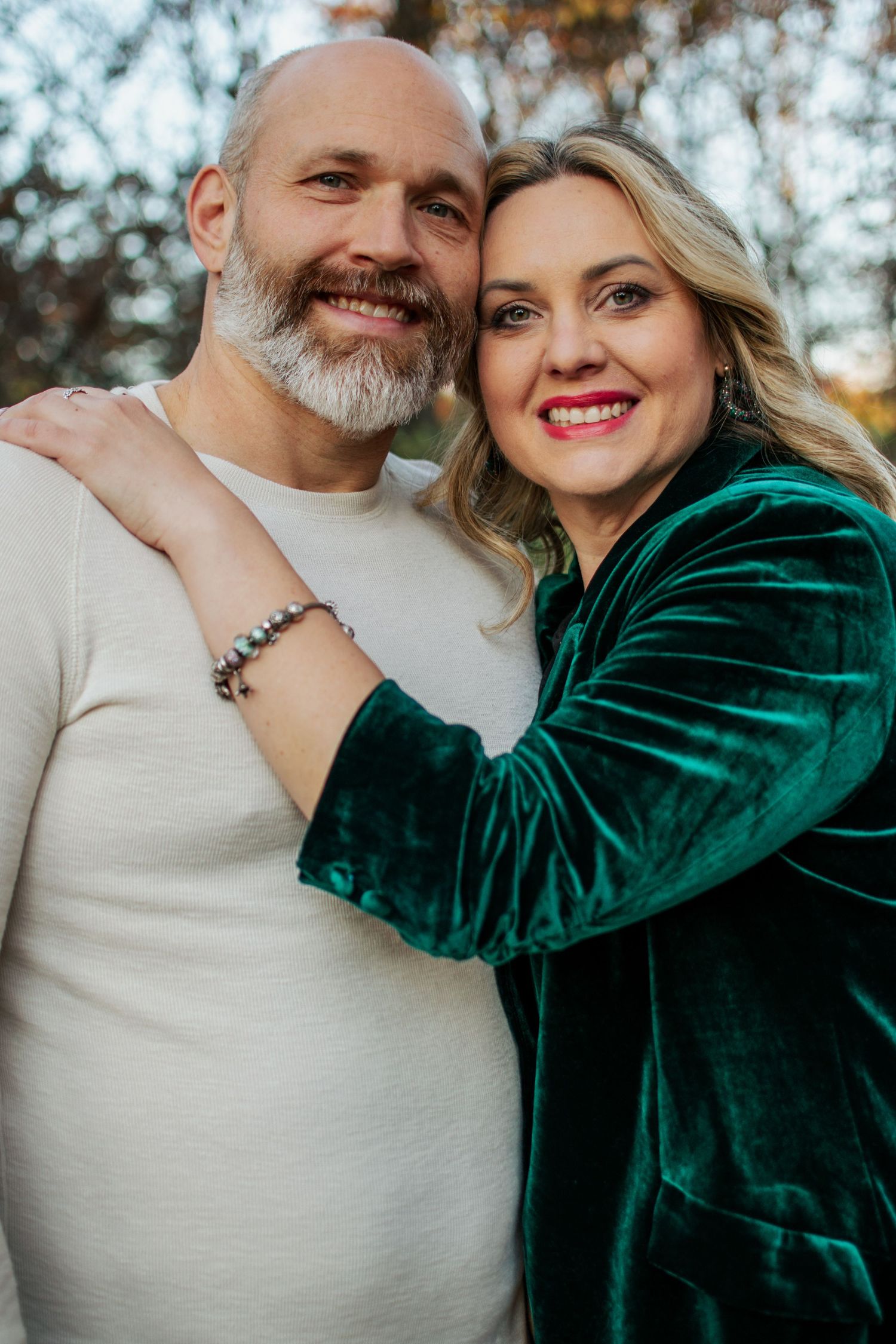A smiling couple embraces outdoors, the woman wearing a green velvet blazer during a fall photo session.